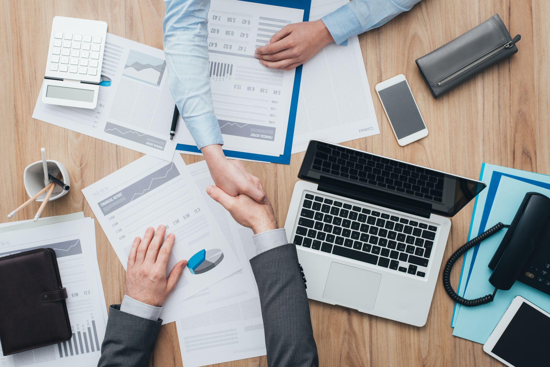 A man and a woman are shaking hands over a table with papers and a laptop.