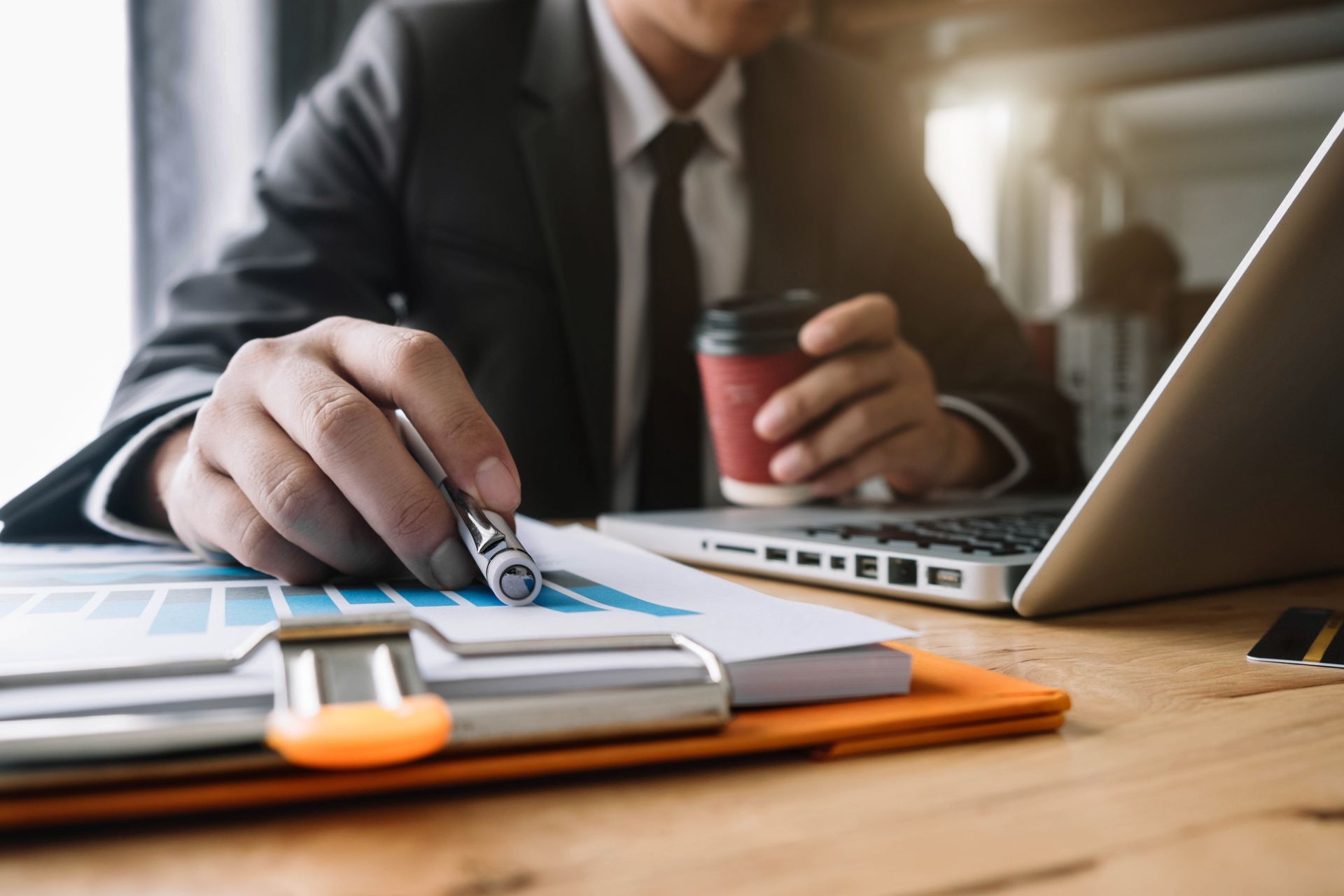 A man is sitting at a desk with a laptop and a cup of coffee.