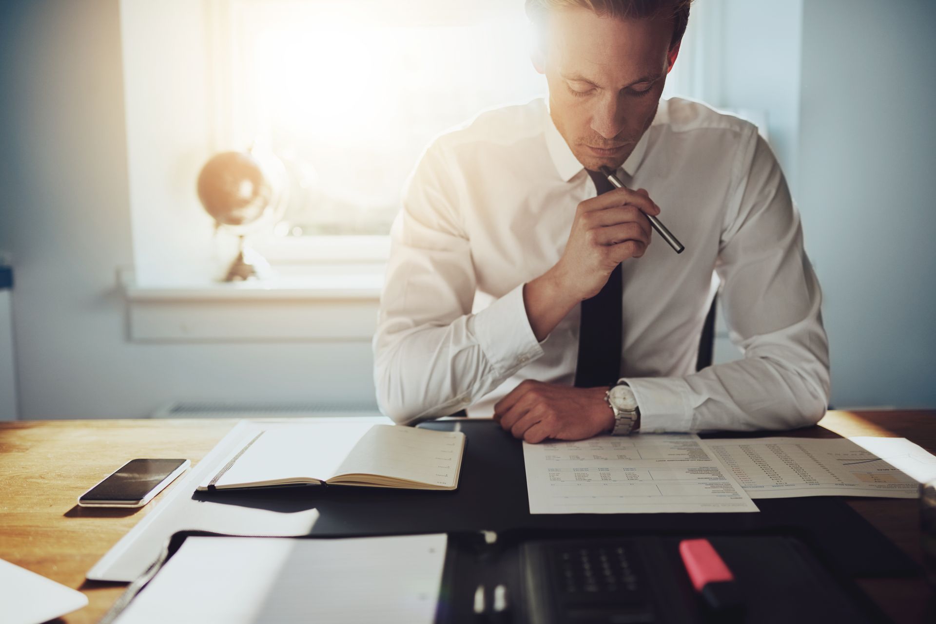A man is sitting at a desk with papers and a pen in his mouth.