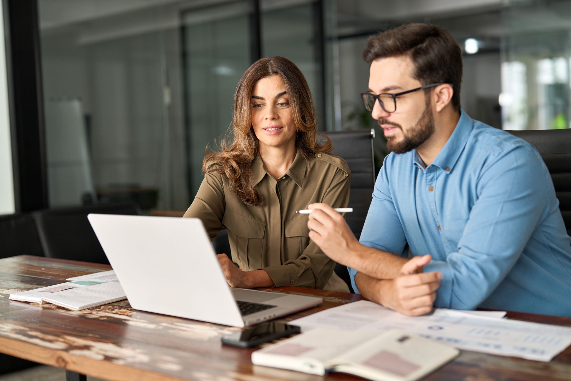 A man and a woman are sitting at a table looking at a laptop computer.