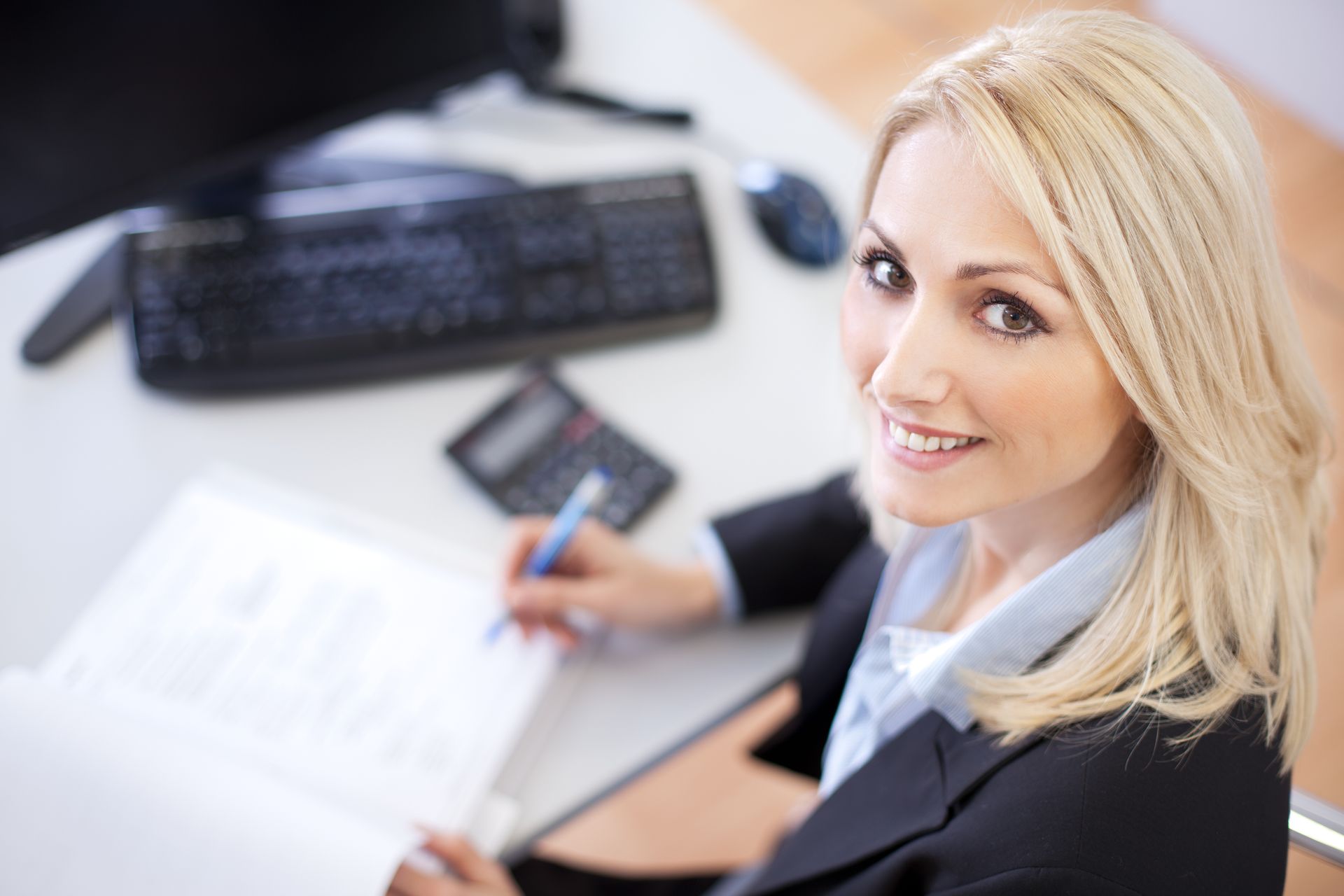 A woman is sitting at a desk with a calculator and a pen