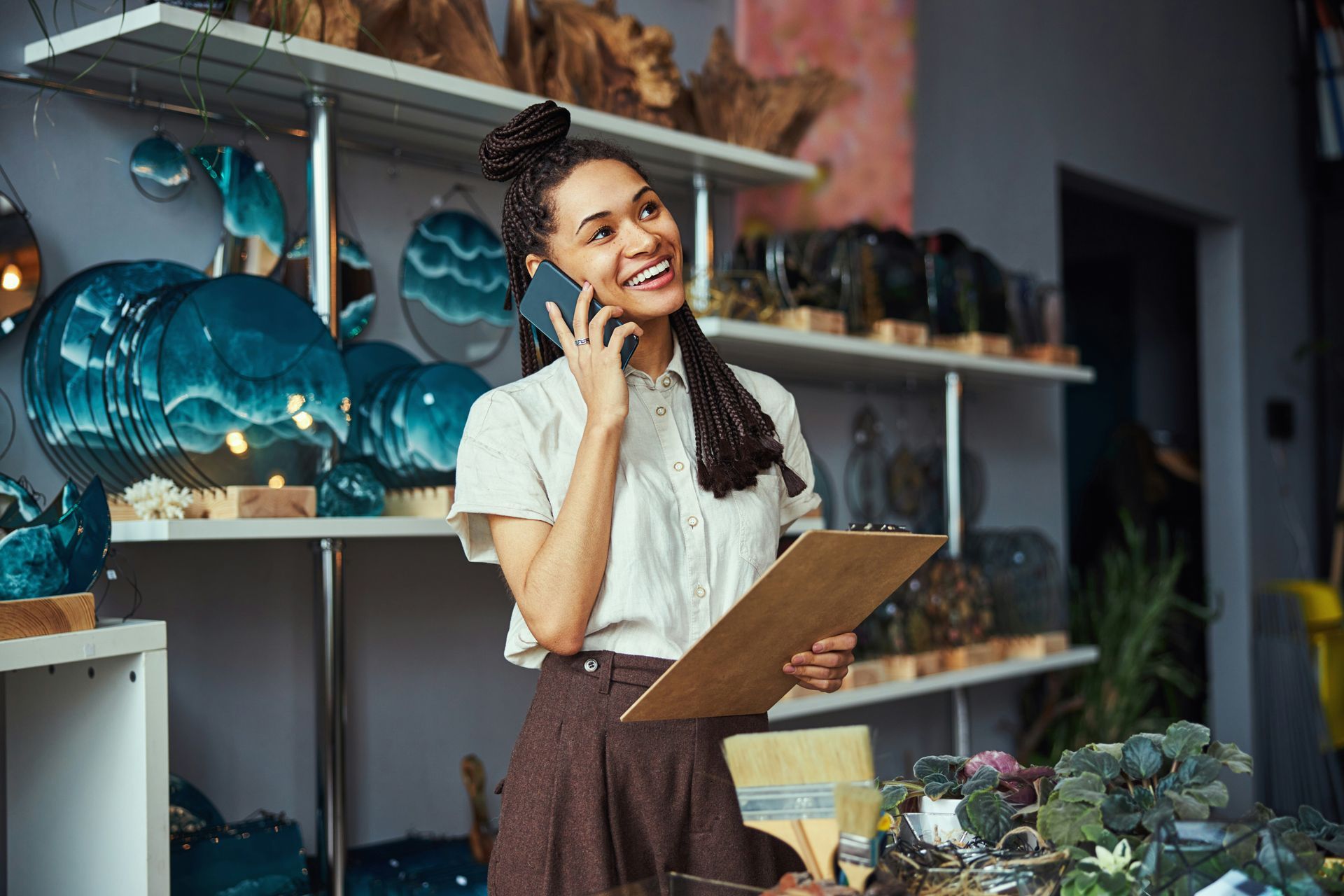 Shop owner on a phone call, smiling while holding a clipboard in a flower and decor shop.