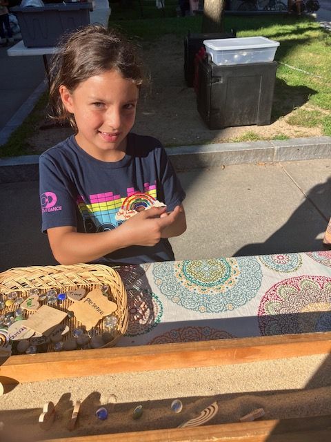 Girl smiles while holding an object; she's at a table with crafts in a basket.