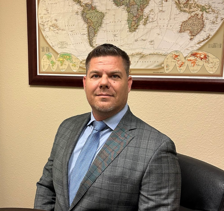 A man in a suit and tie is sitting in front of a map of the world.