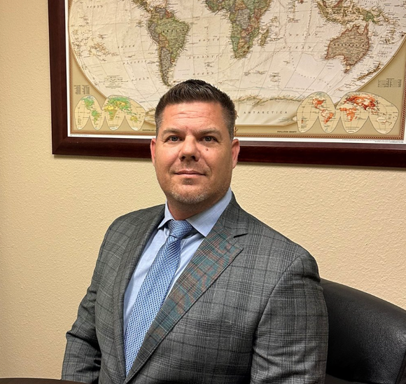 A man in a suit and tie is sitting in front of a map of the world.