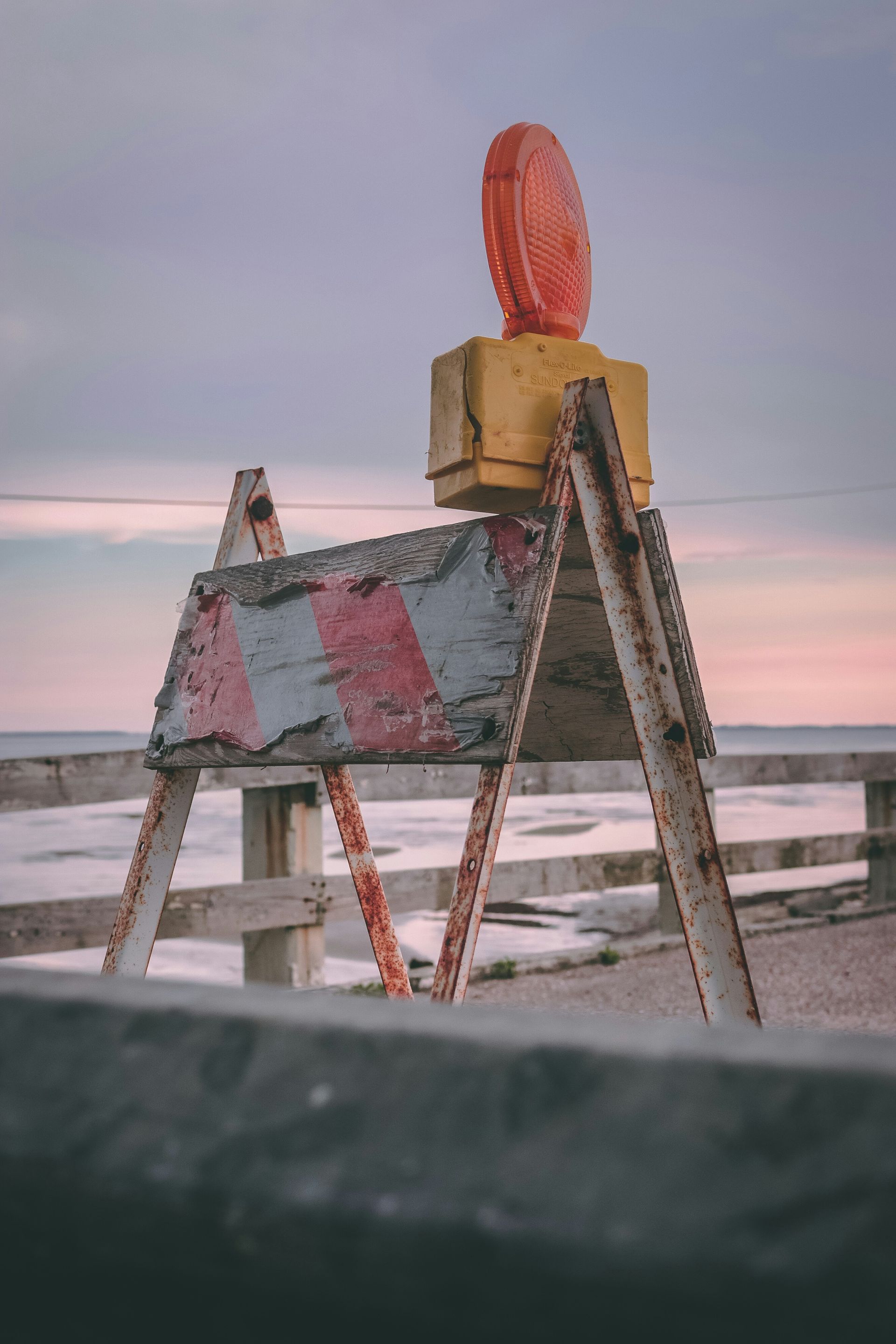 A construction sign is sitting on top of a wooden fence next to the ocean.