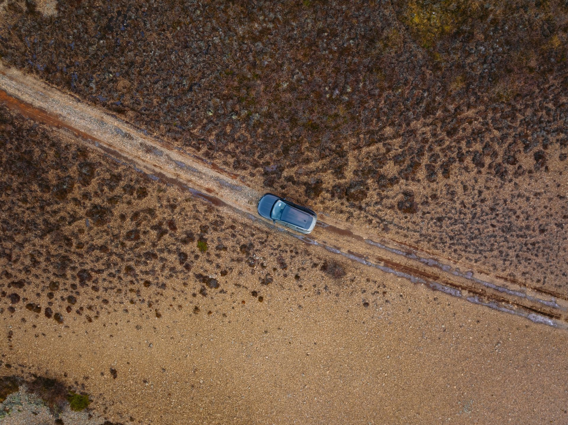 An aerial view of a car driving down a dirt road.