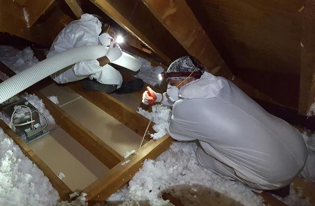 A man is working in an attic with a ceiling fan.