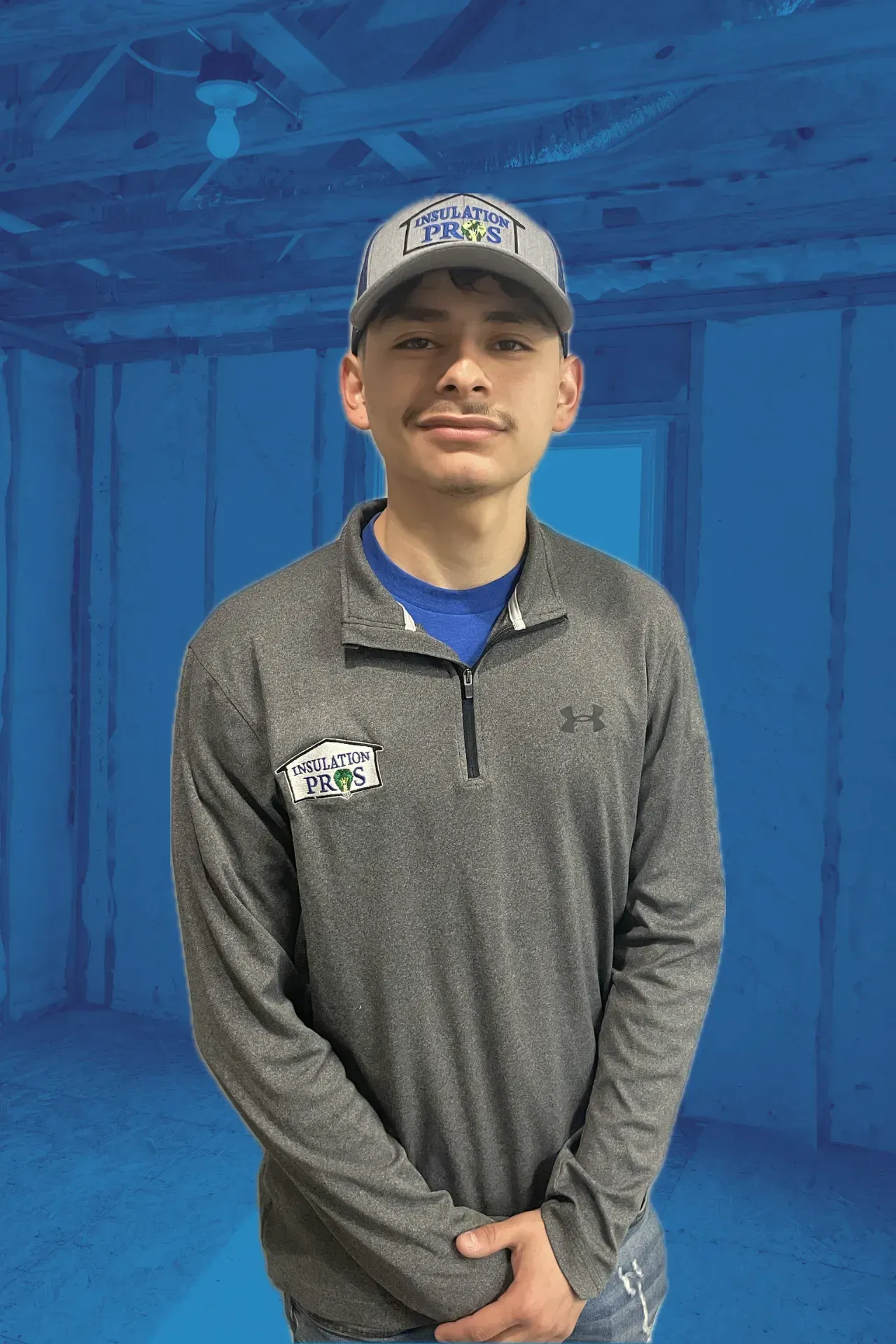 A young man wearing a hat and a gray shirt is standing in front of a blue wall.