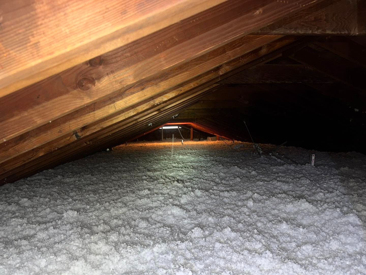 Attic space filled with loose, white insulation between wooden rafters.