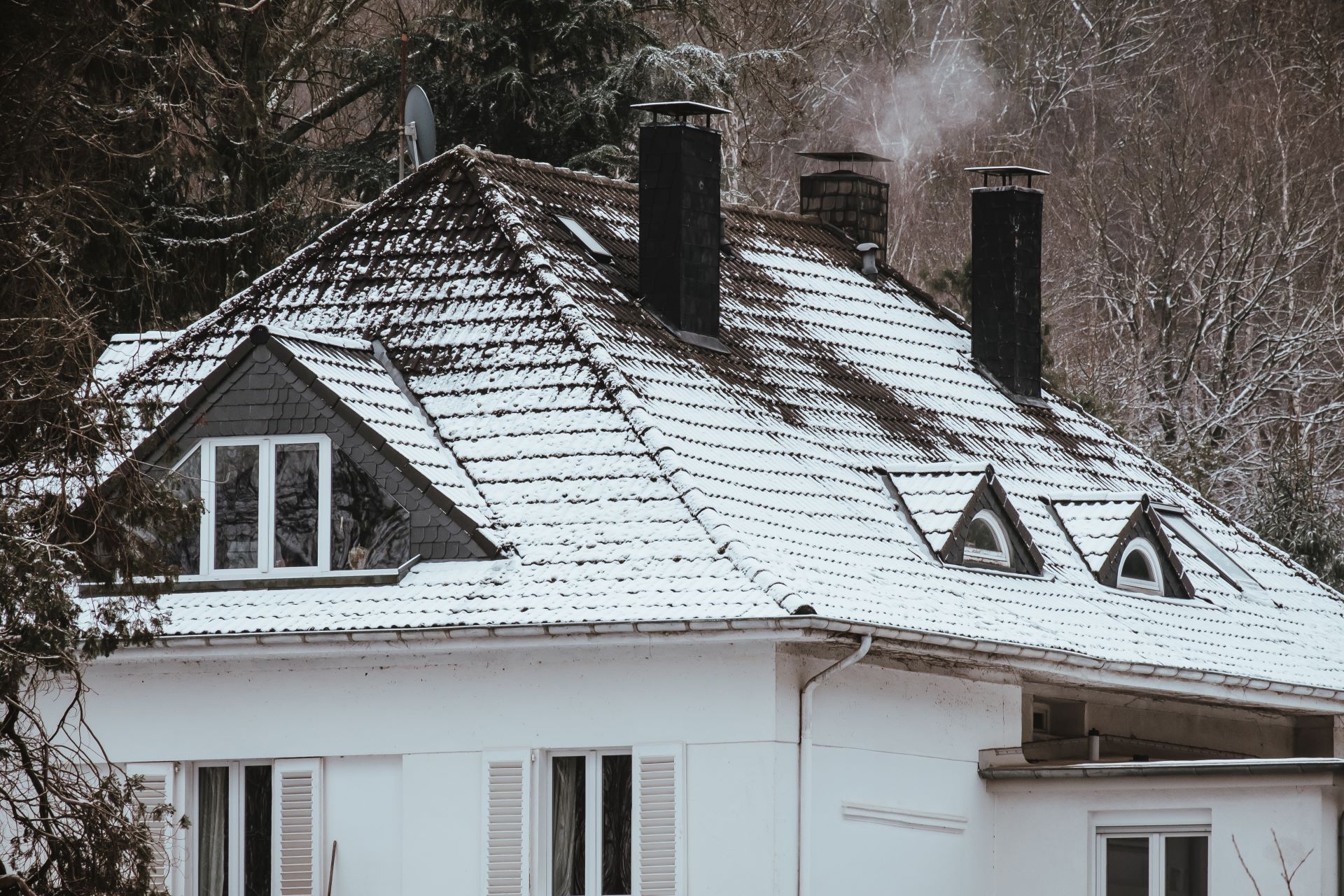Snow-covered house with dormers and chimneys; smoke rising. Winter scene.