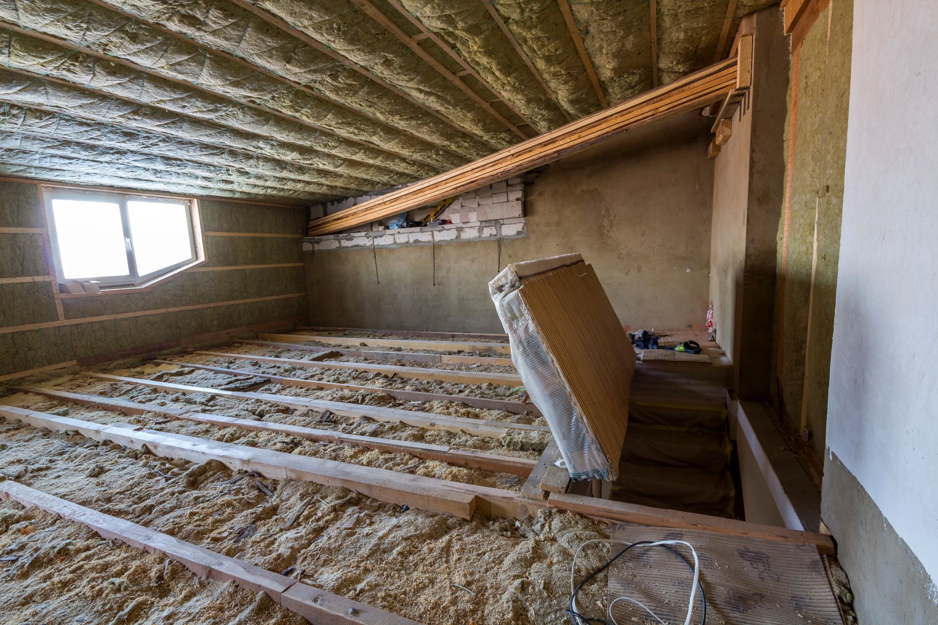 Interior of a room under construction with exposed wooden beams, insulation, and unfinished walls.