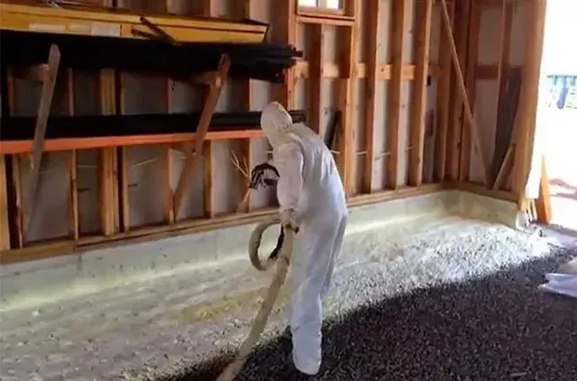 A man is spraying foam on the floor of a building.