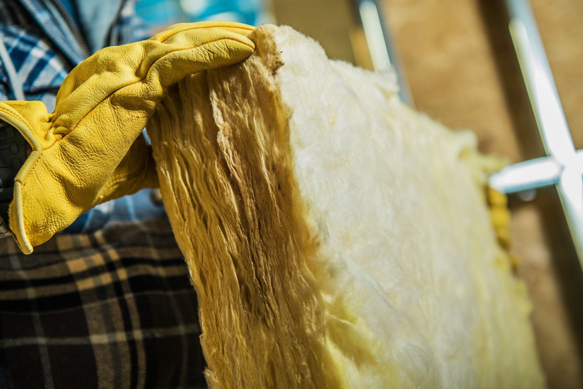 Person wearing yellow gloves holds insulation board in an unfinished room.