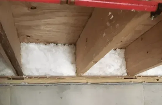 A close up of a piece of insulation between two wooden beams in a room.