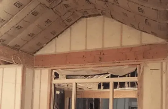 A room in a house under construction with a vaulted ceiling and a window.