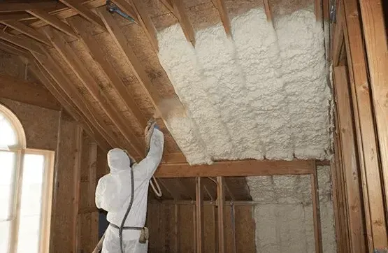 A man is spraying foam on the ceiling of a house.