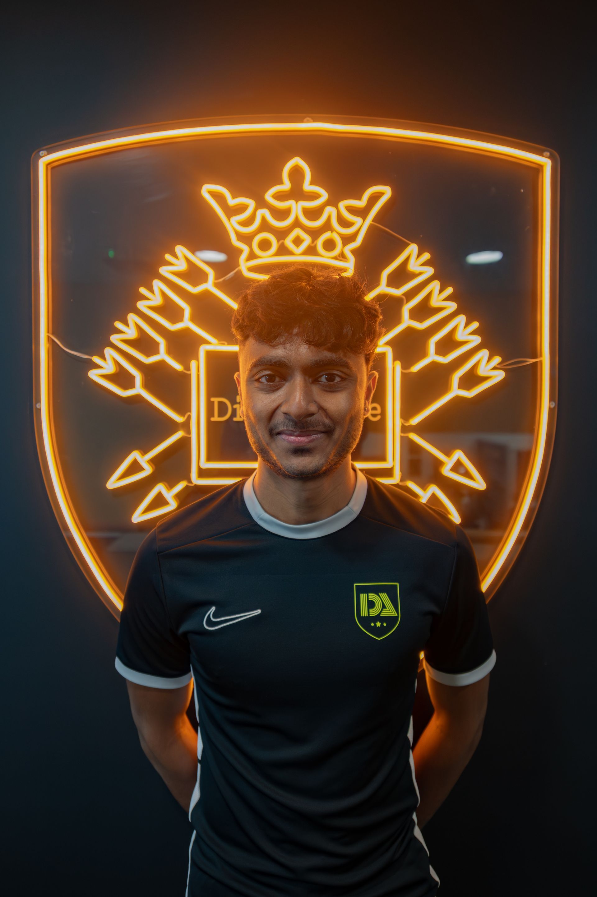 Soccer player in black and green jersey smiles, standing in front of a neon gold crest.