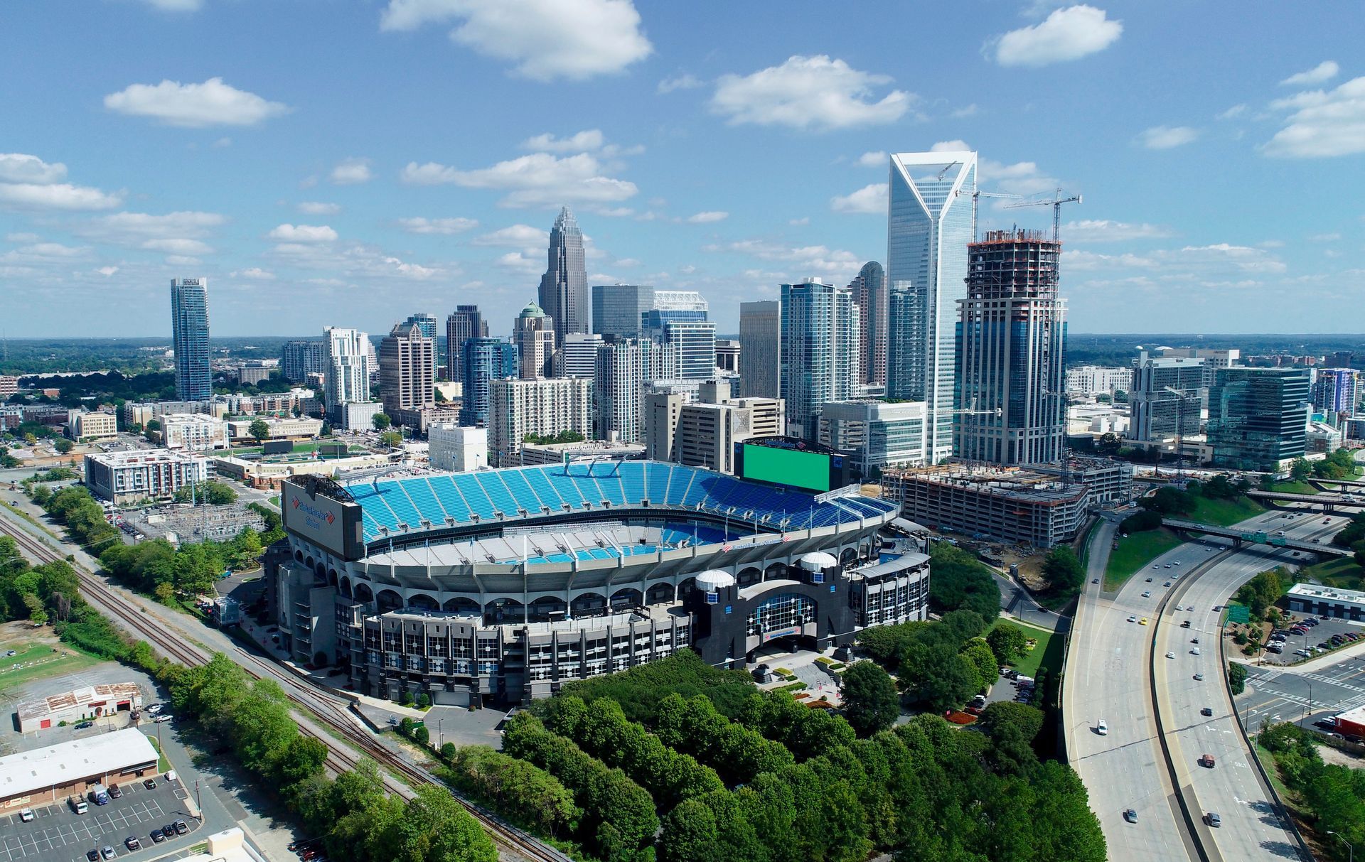 Aerial view of Bank of America Stadium in Charlotte, NC, with the city skyline in the background on a sunny day.
