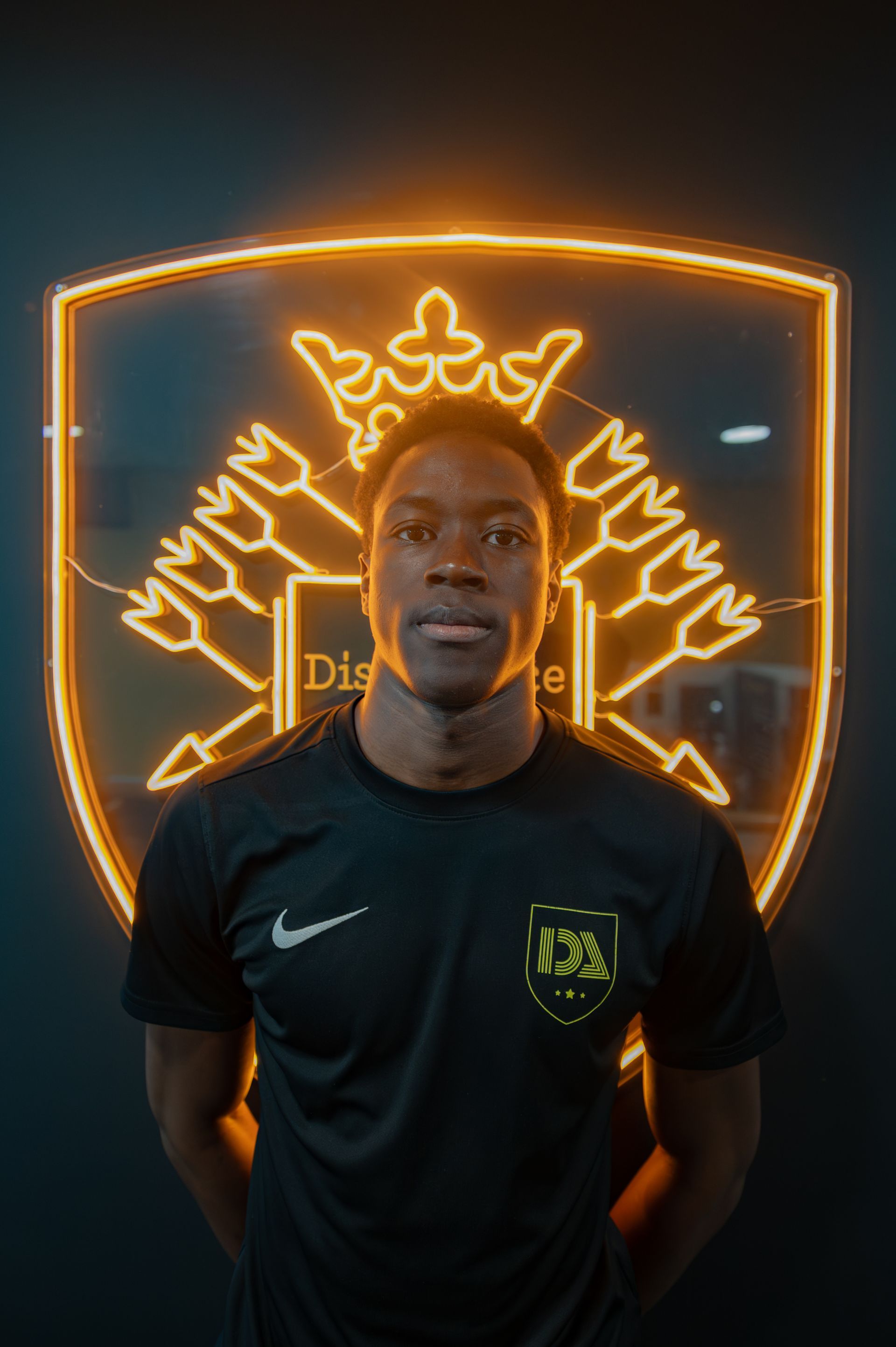 Soccer player in black jersey stands before a lit gold team emblem.