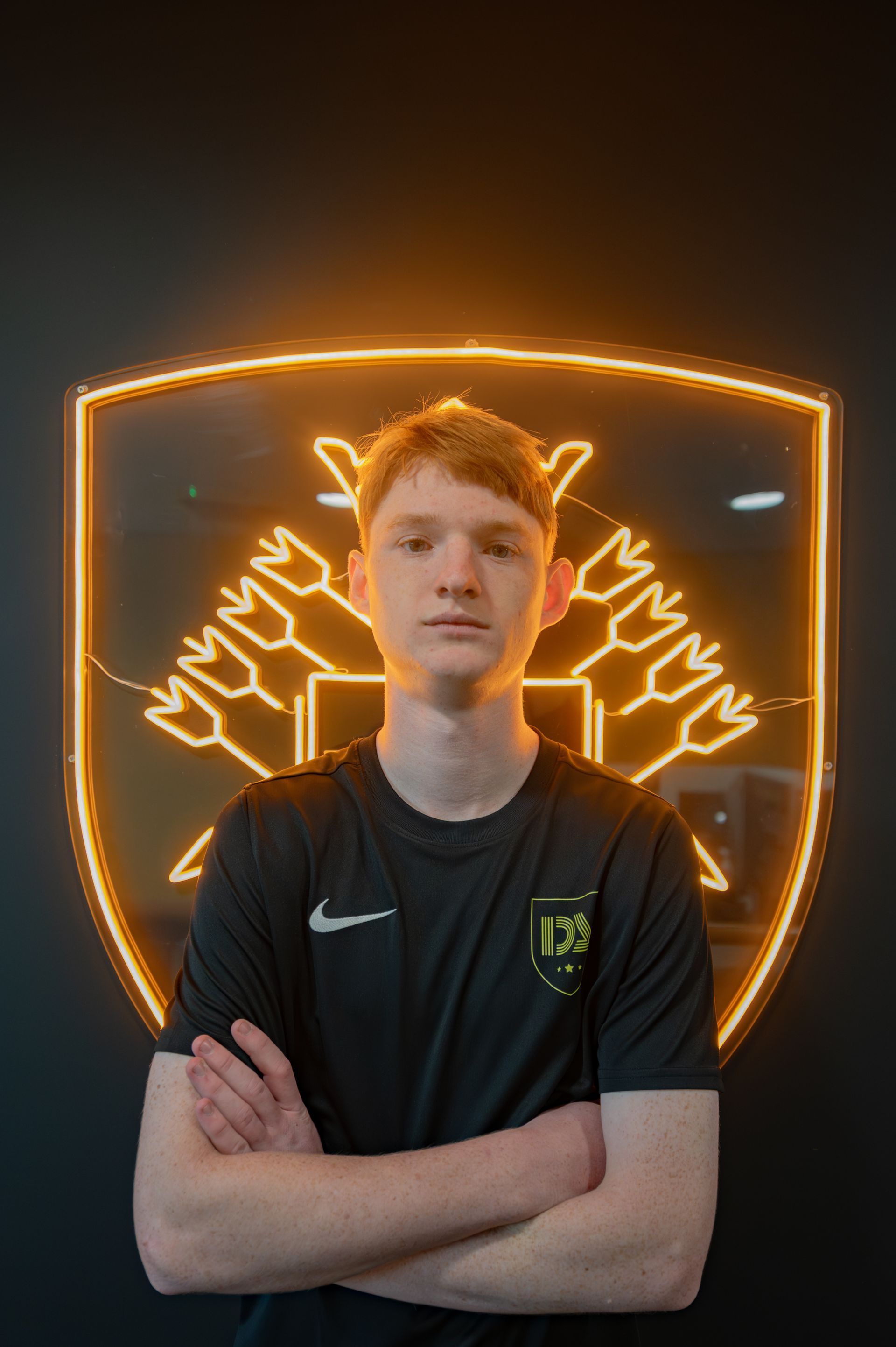 Young person with arms crossed in front of a glowing shield logo.