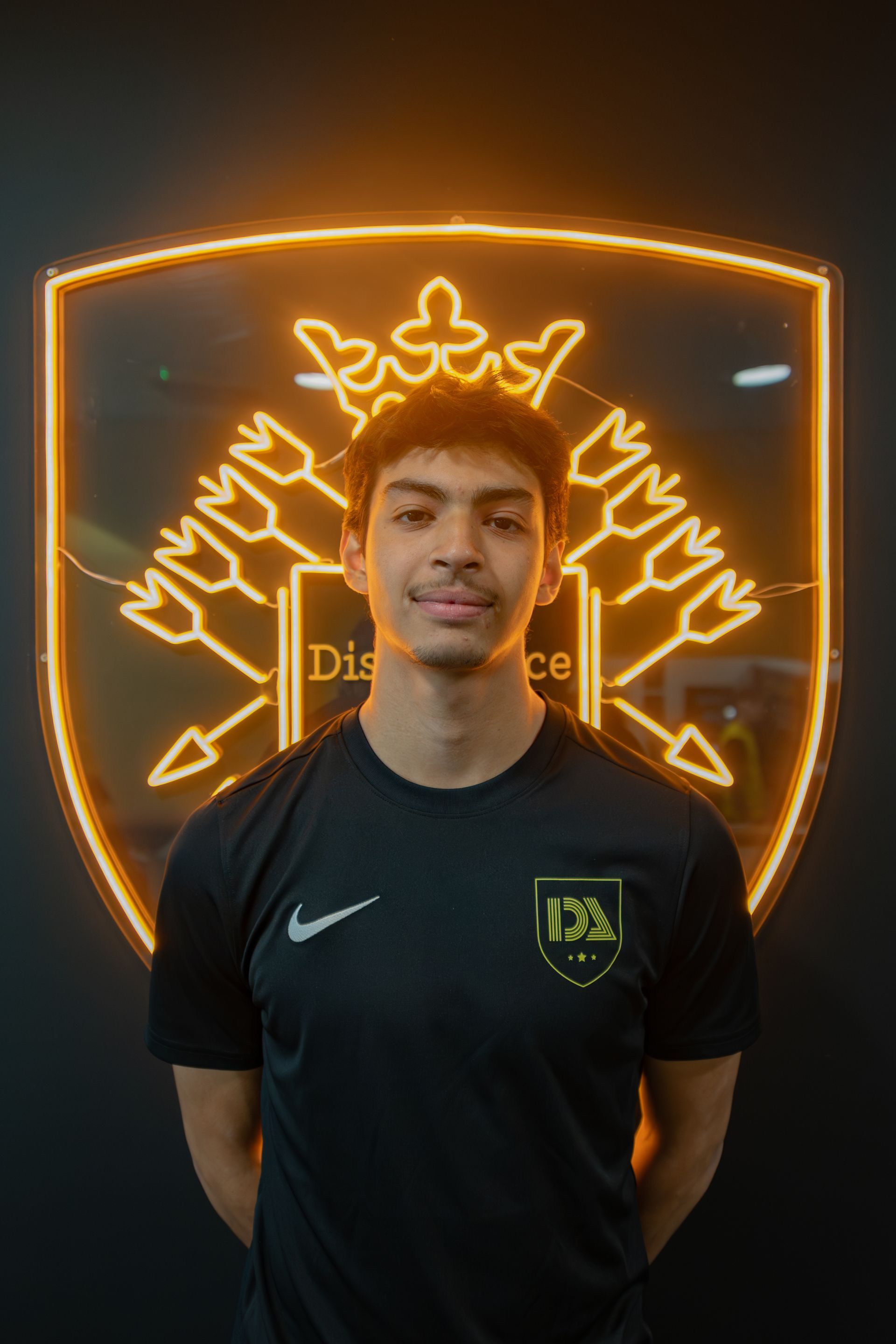 Young person in black shirt smiling in front of a glowing logo with arrows.