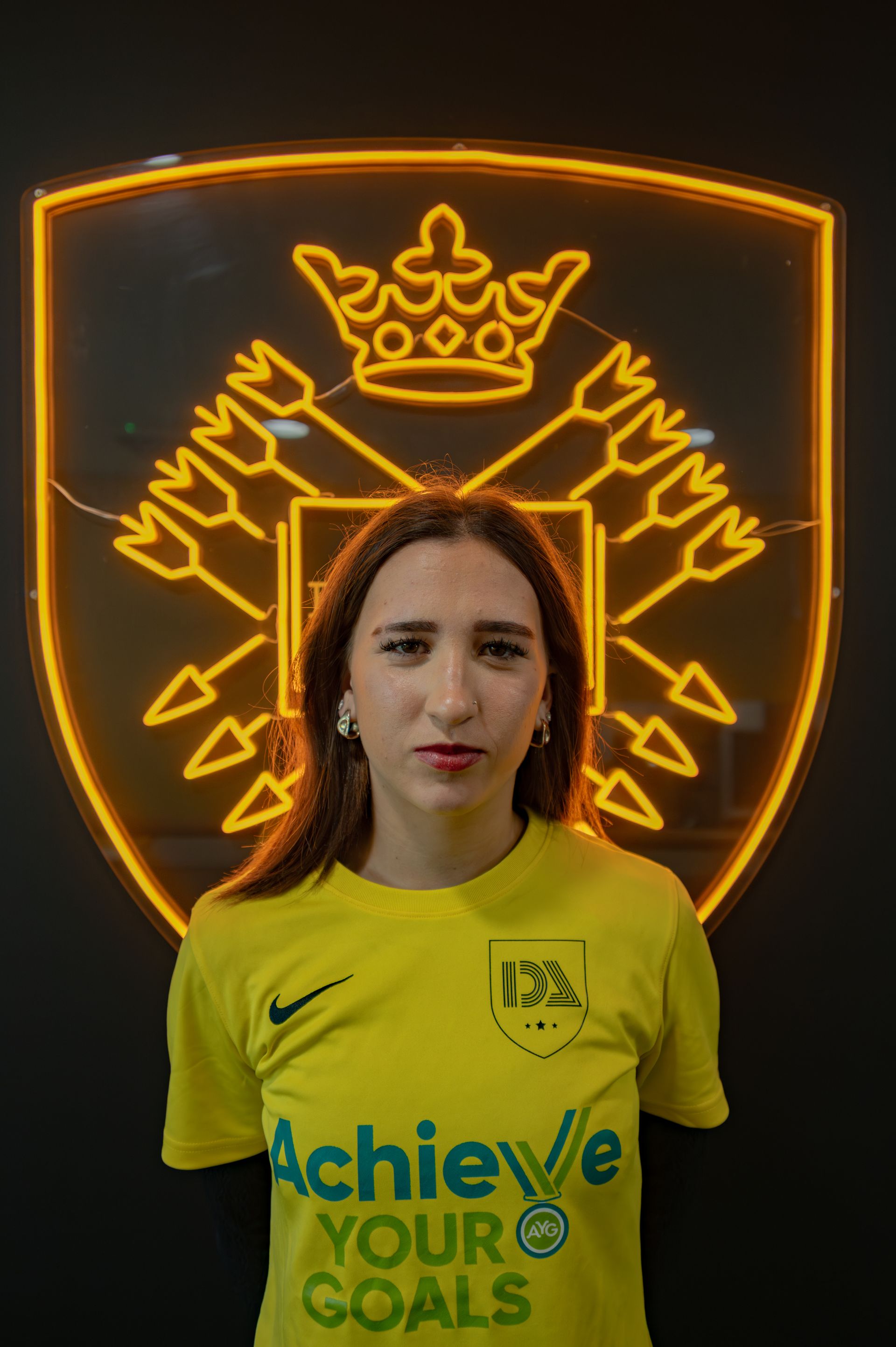 Woman in yellow shirt in front of neon logo. The shirt says 