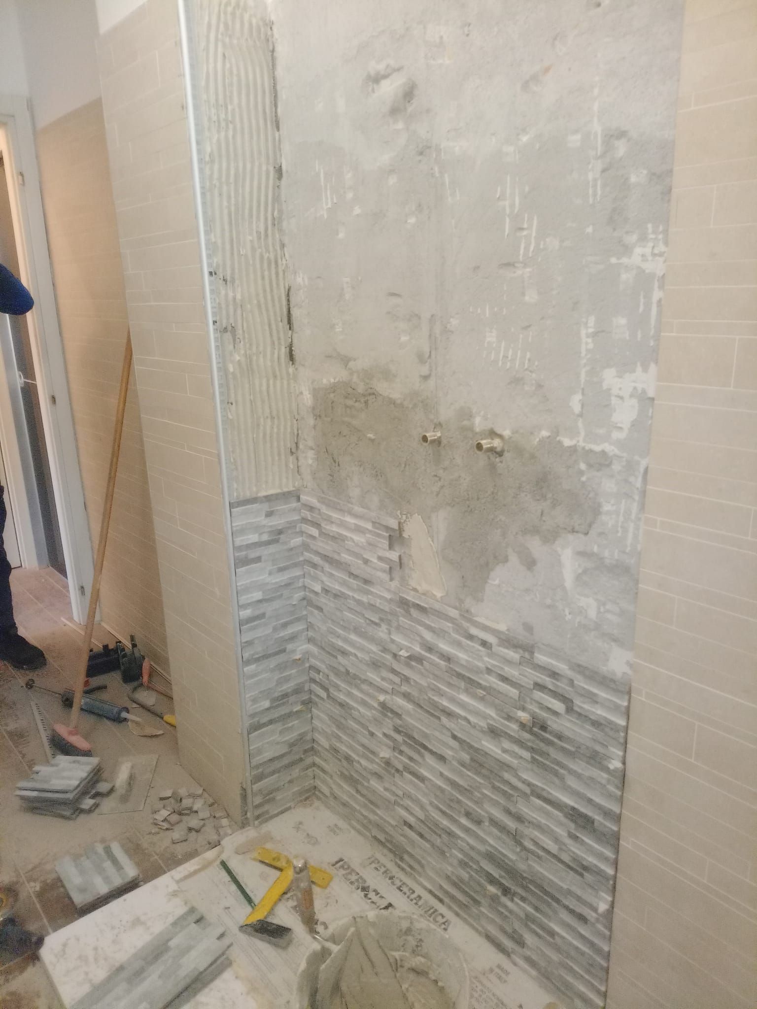 Un uomo sta posando delle piastrelle su un muro in un bagno.