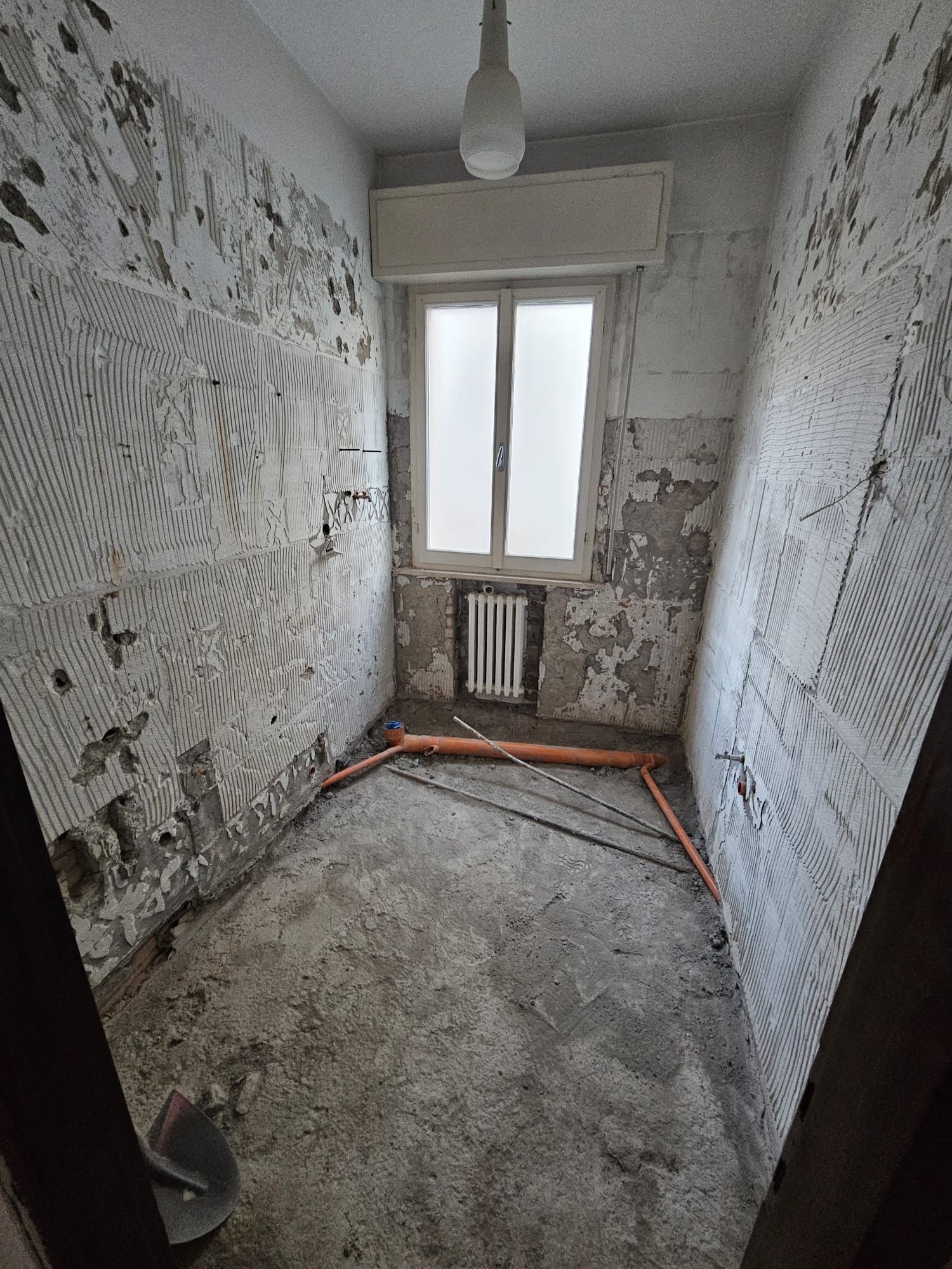 Una stanza con una finestra e un termosifone è in fase di ristrutturazione.