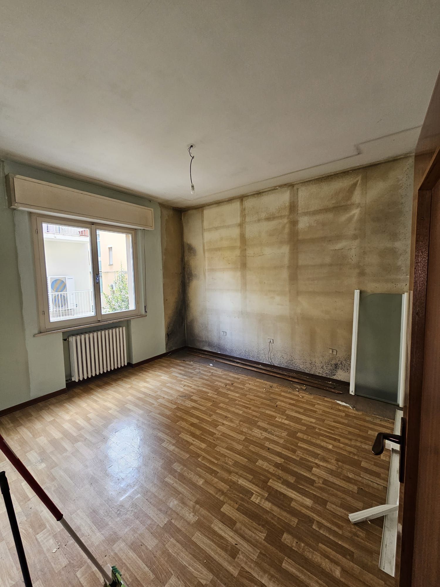 Una stanza vuota con pavimento in legno e una finestra.