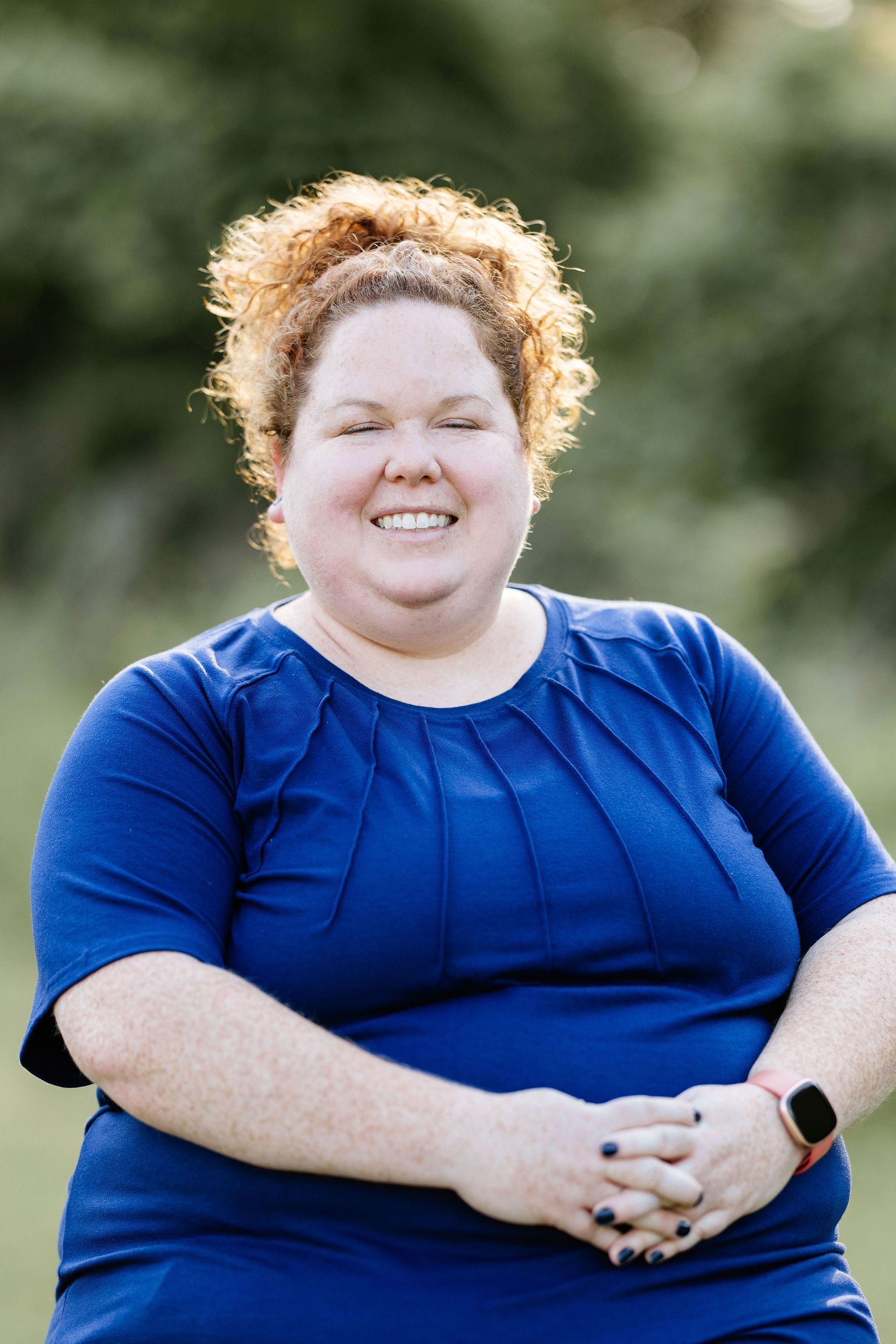 Woman in blue top smiles outdoors.
