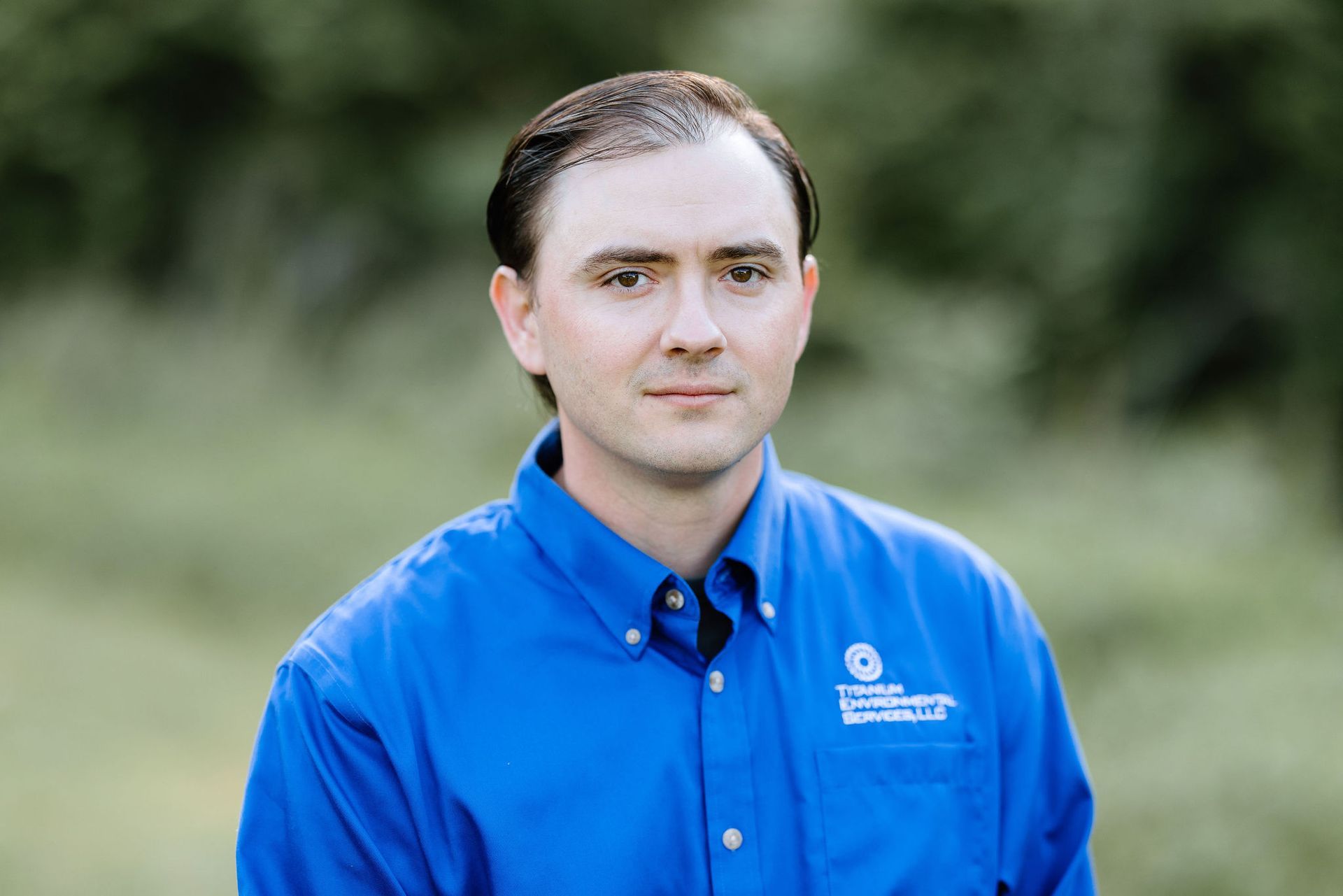 Man in blue shirt, light skin, looking at camera. Outdoors, green background.