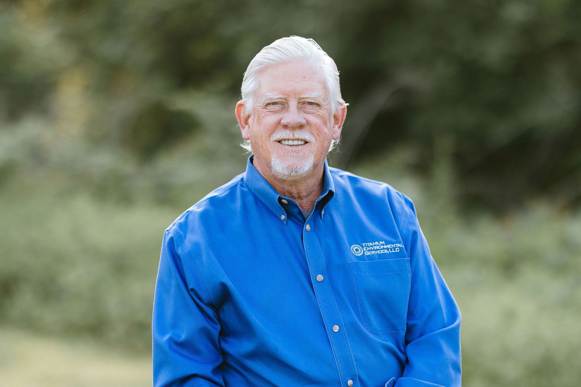 Smiling man in blue shirt, outdoors, blurred background.