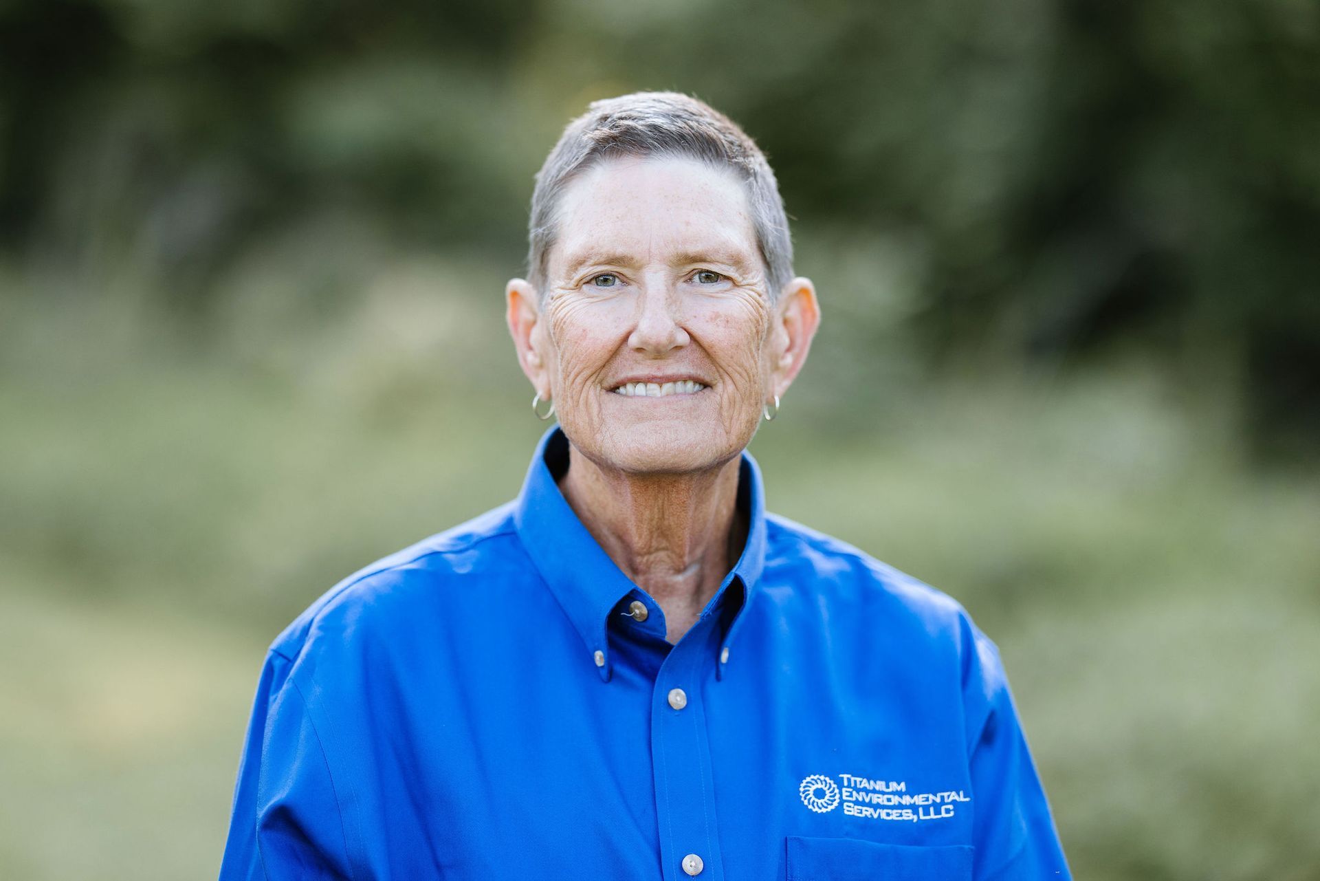 Person wearing a blue shirt with logo, smiling, outdoors.