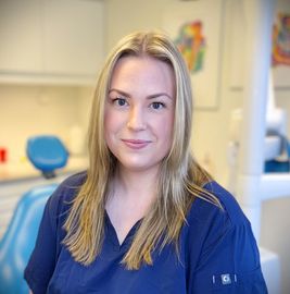 Tannlege Christian med briller og skjegg, iført blå skjorte og medisinsk maske, smiler til kameraet.