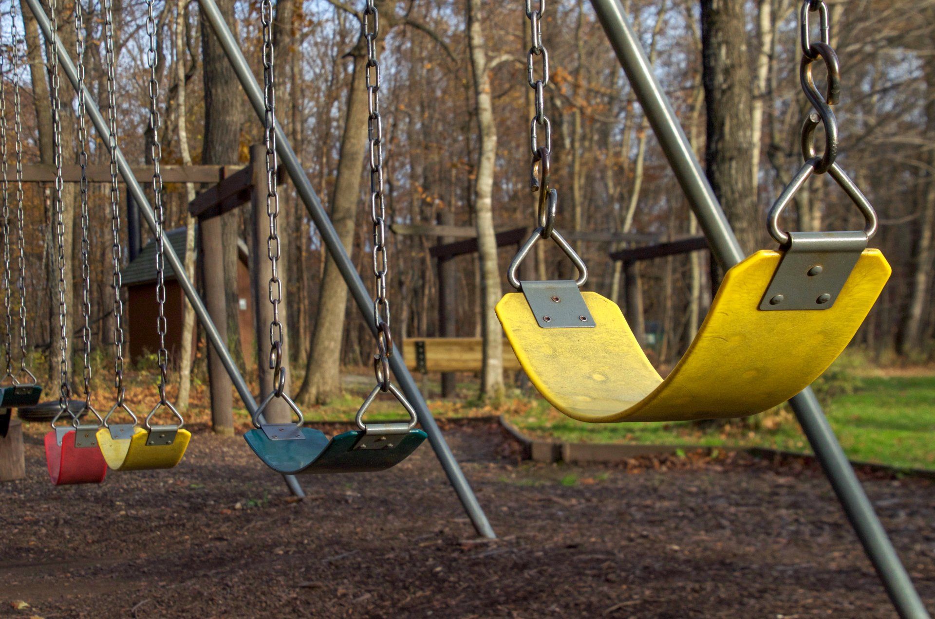A row of colorful swings in a park with trees in the background