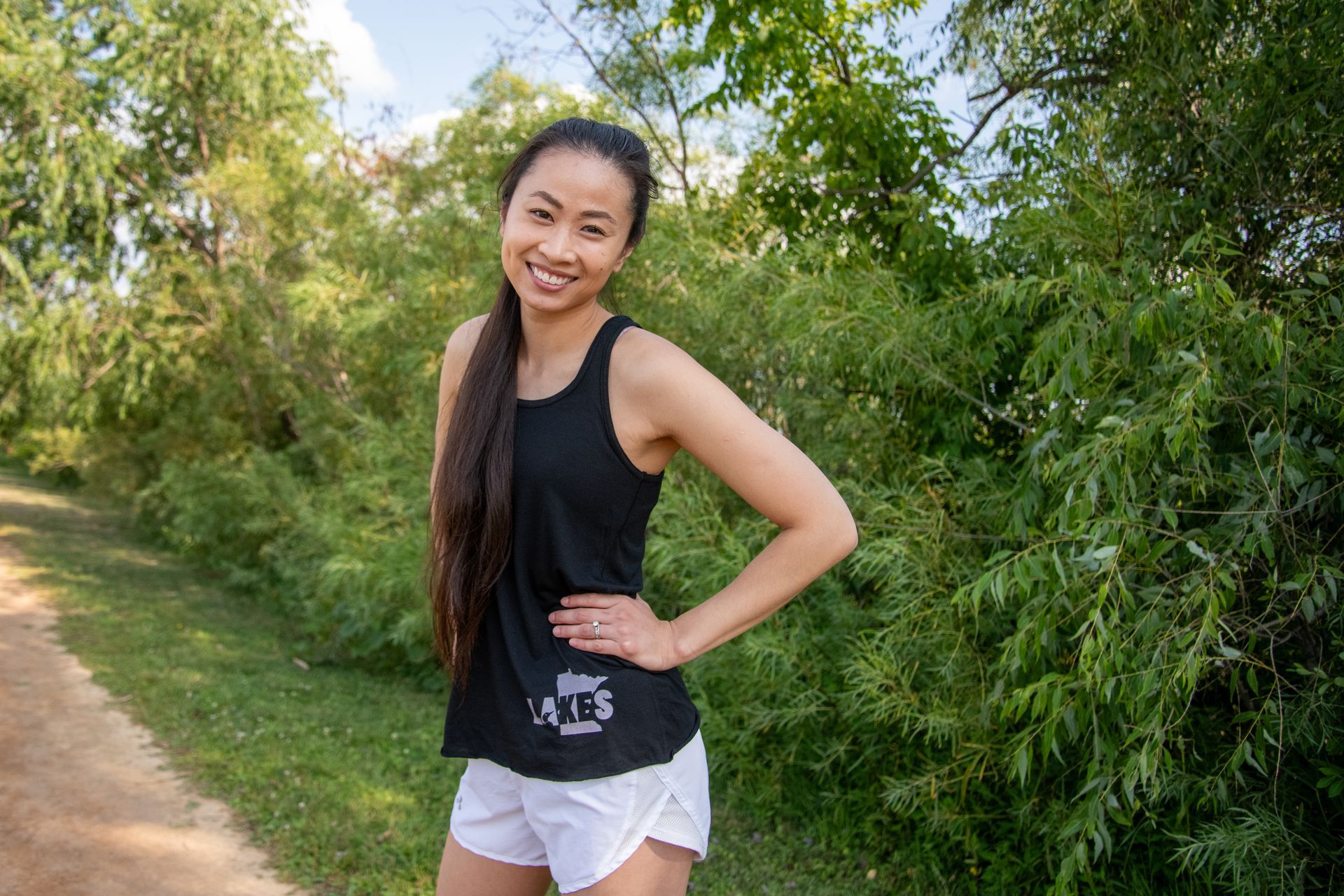 A woman in a black tank top and white shorts is standing on a dirt path