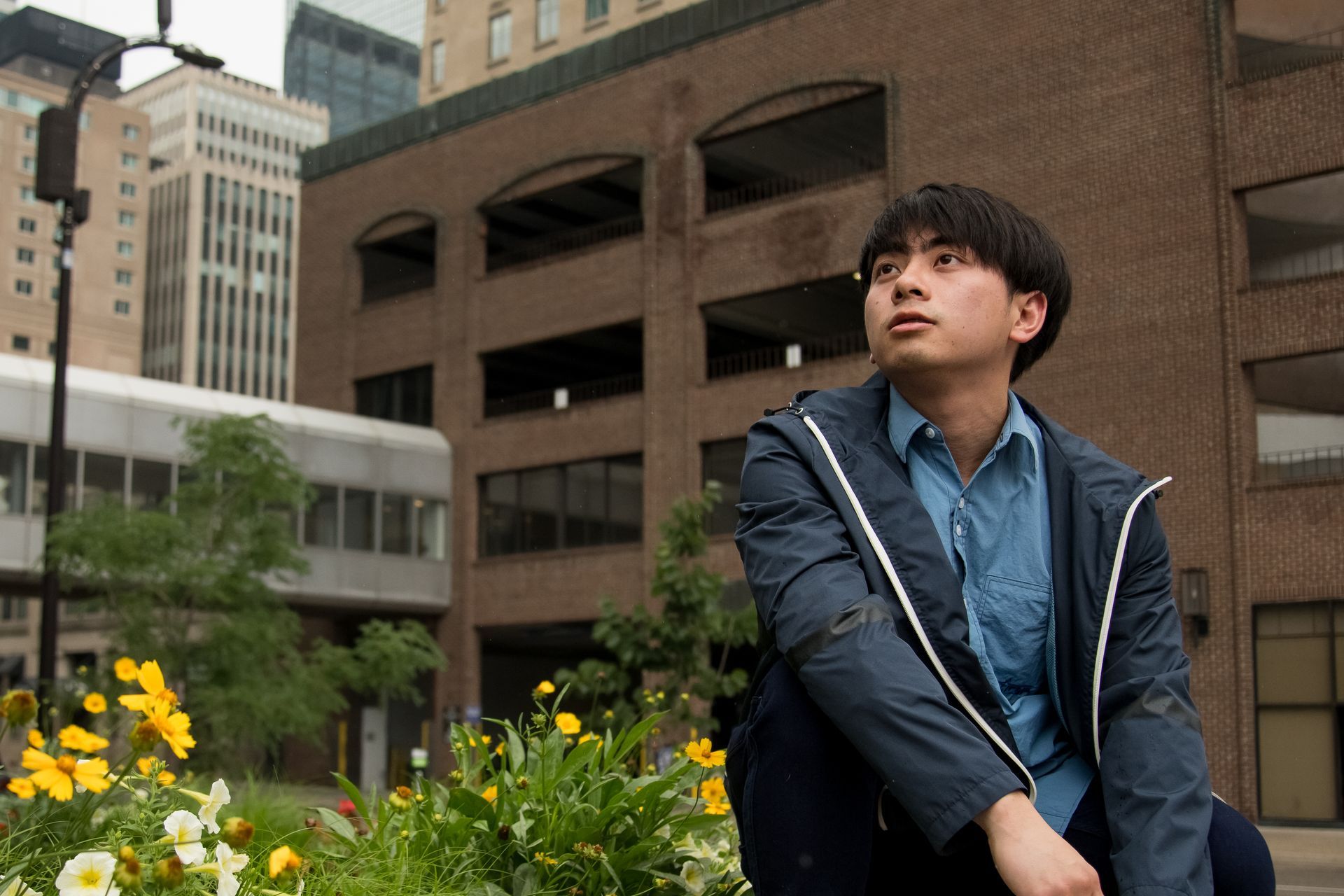 A man in a blue jacket sits in front of a brick building