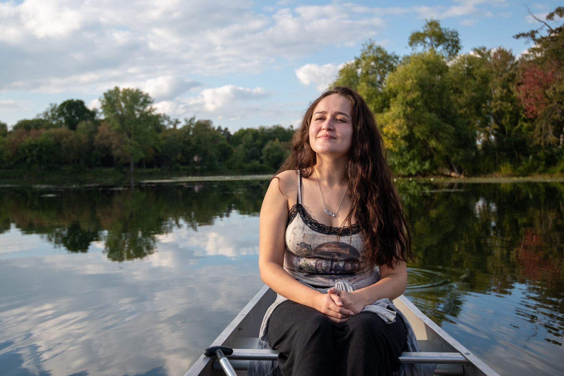 A woman sits in a boat on a lake with her eyes closed