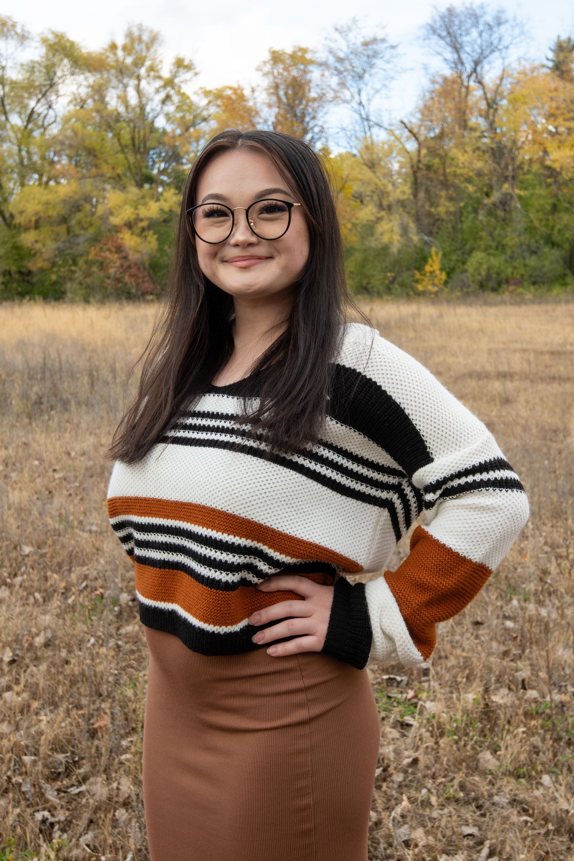 A woman wearing glasses and a striped sweater is standing in a field.
