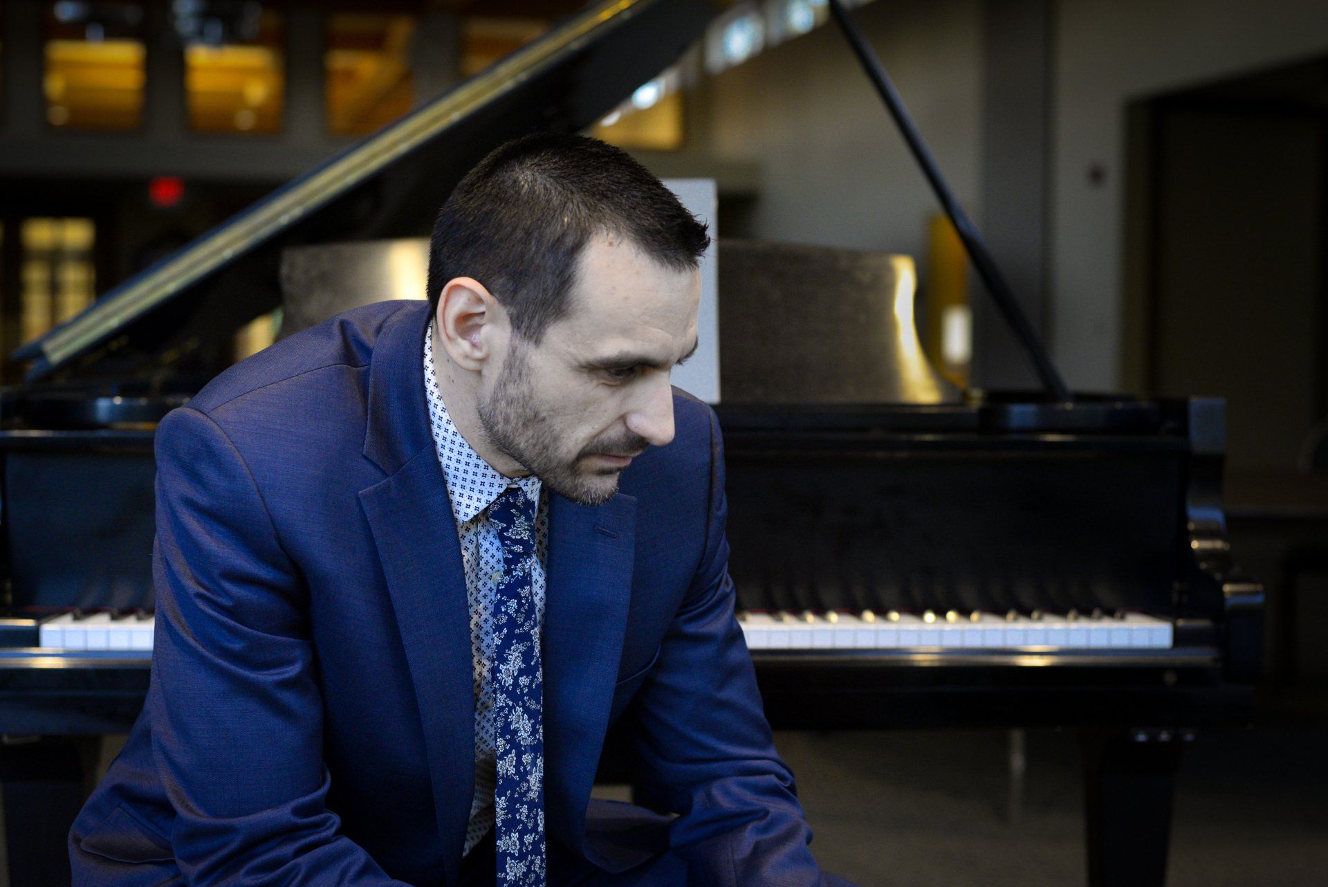 A man in a suit and tie sits in front of a piano