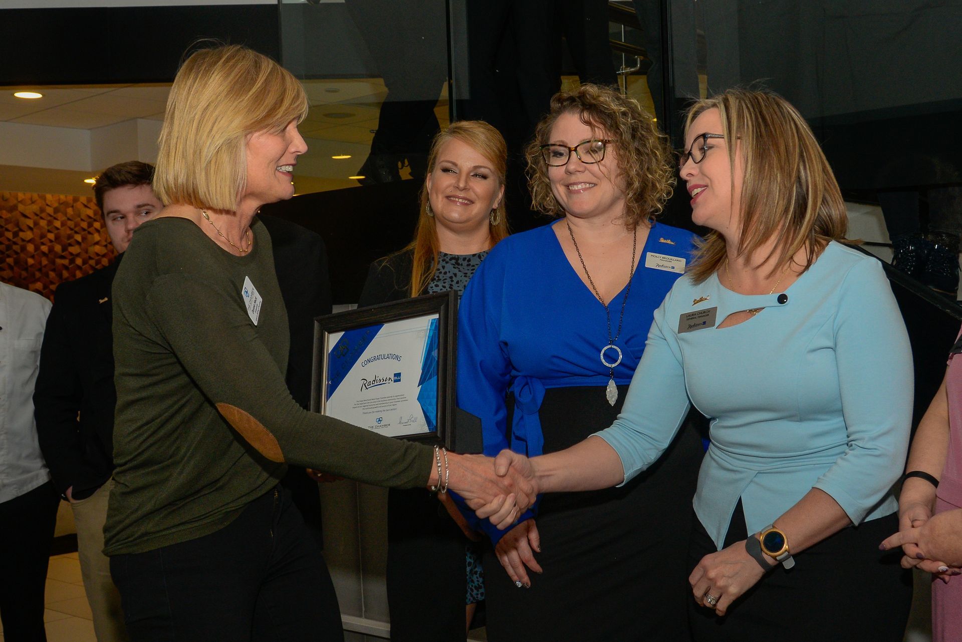 A woman is shaking hands with another woman while holding a framed picture