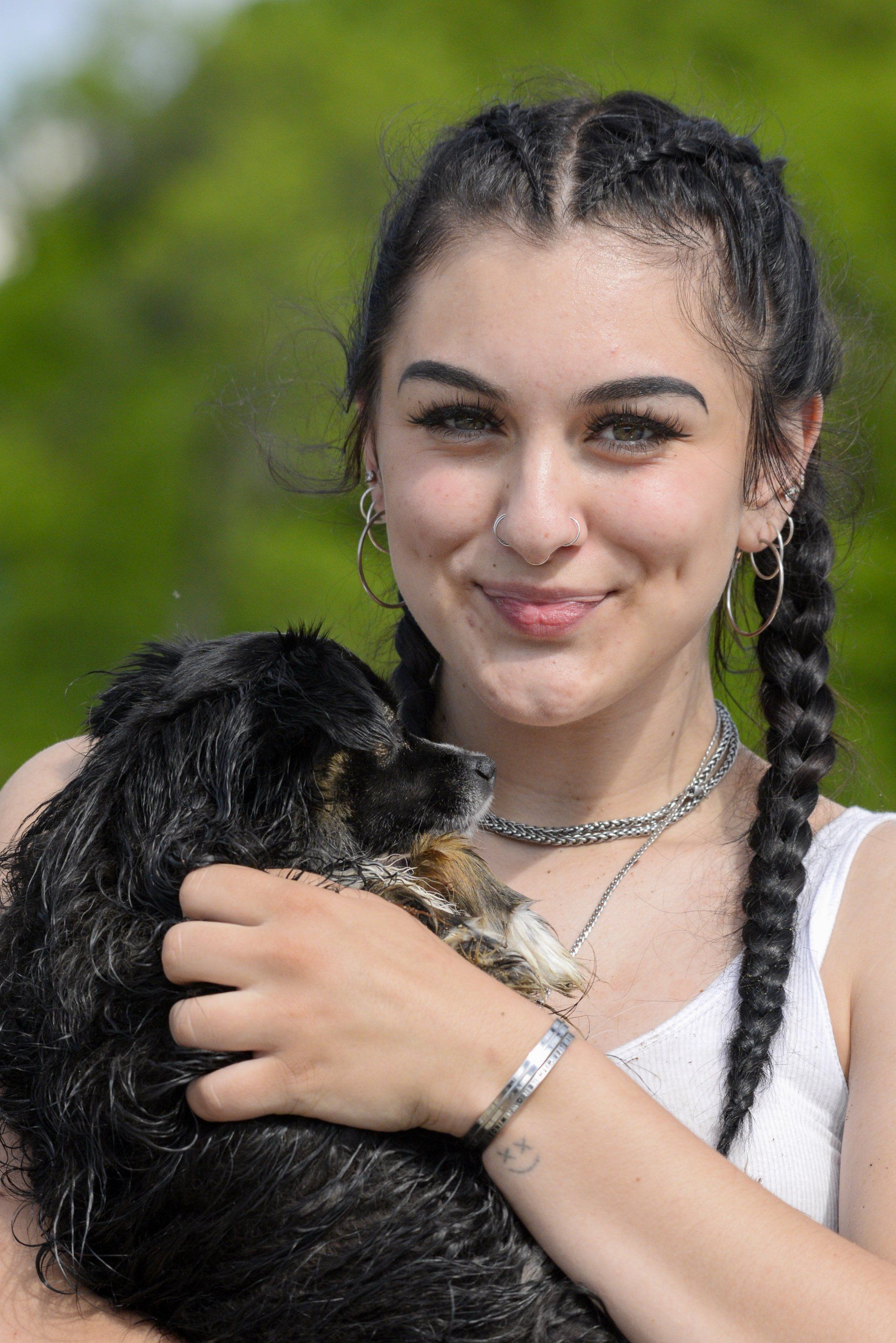 A woman with braids is holding a black cat in her arms.