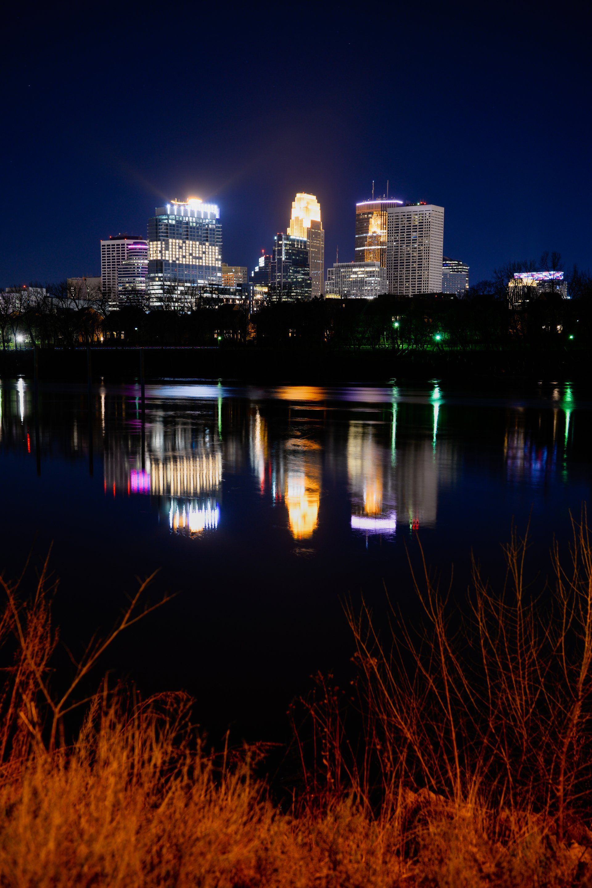 A city skyline is reflected in a body of water at night
