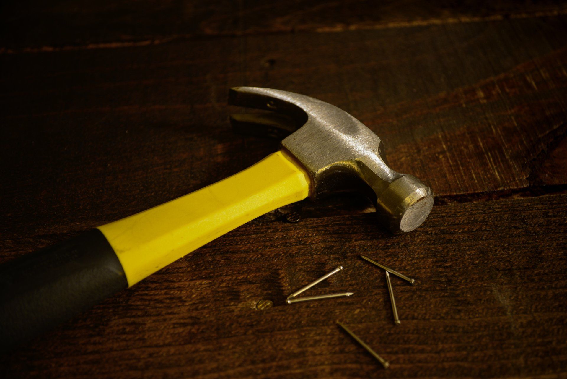 A hammer with a yellow handle is laying on a wooden surface
