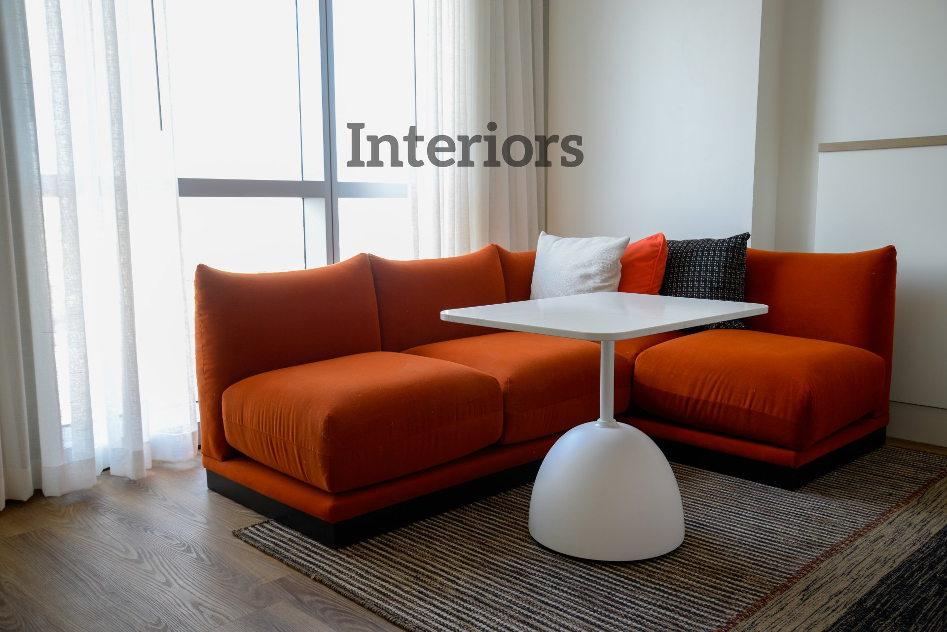 A living room with an orange sectional couch and a white table under the words interiors