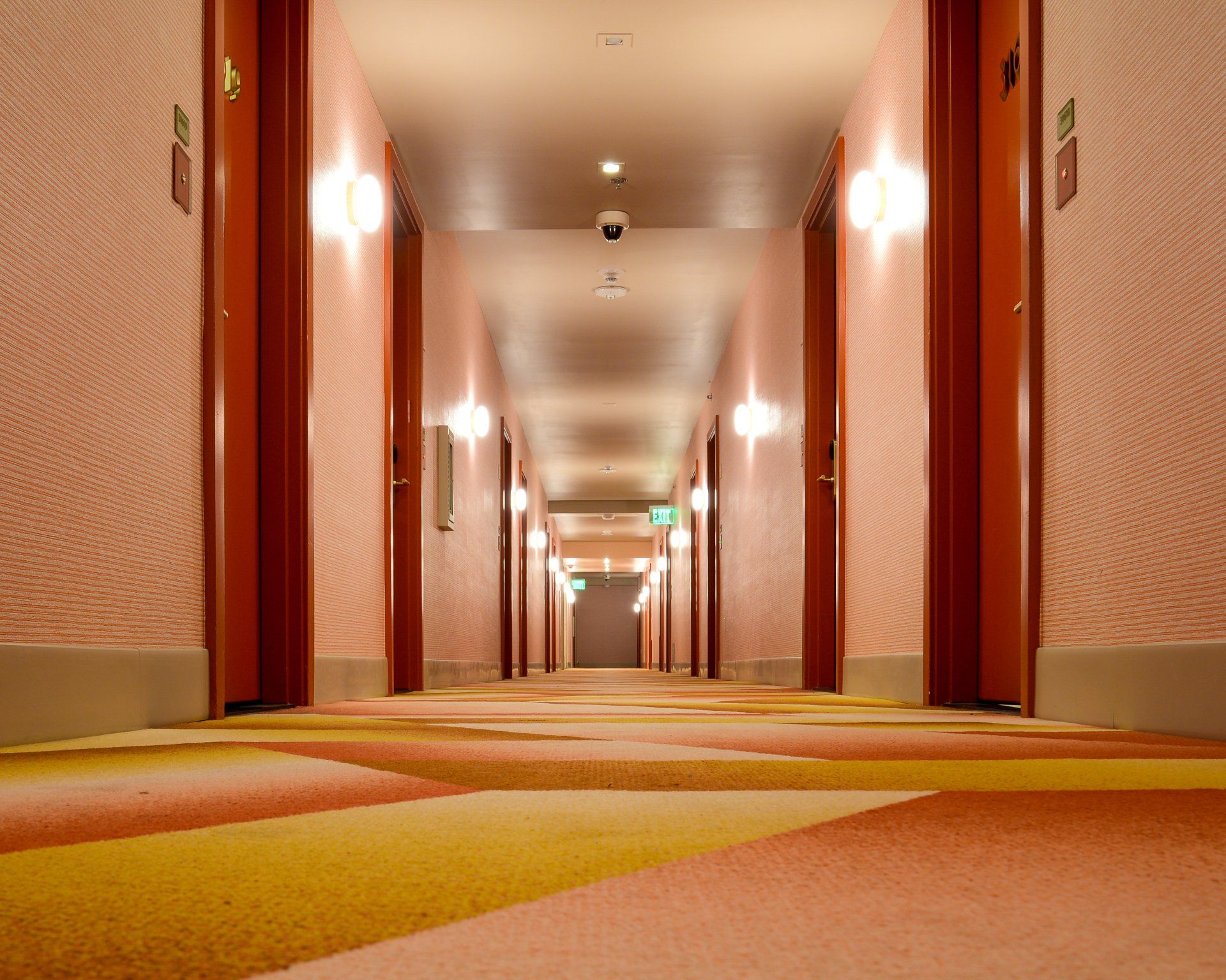 A long hallway in a hotel with a green exit sign on the ceiling