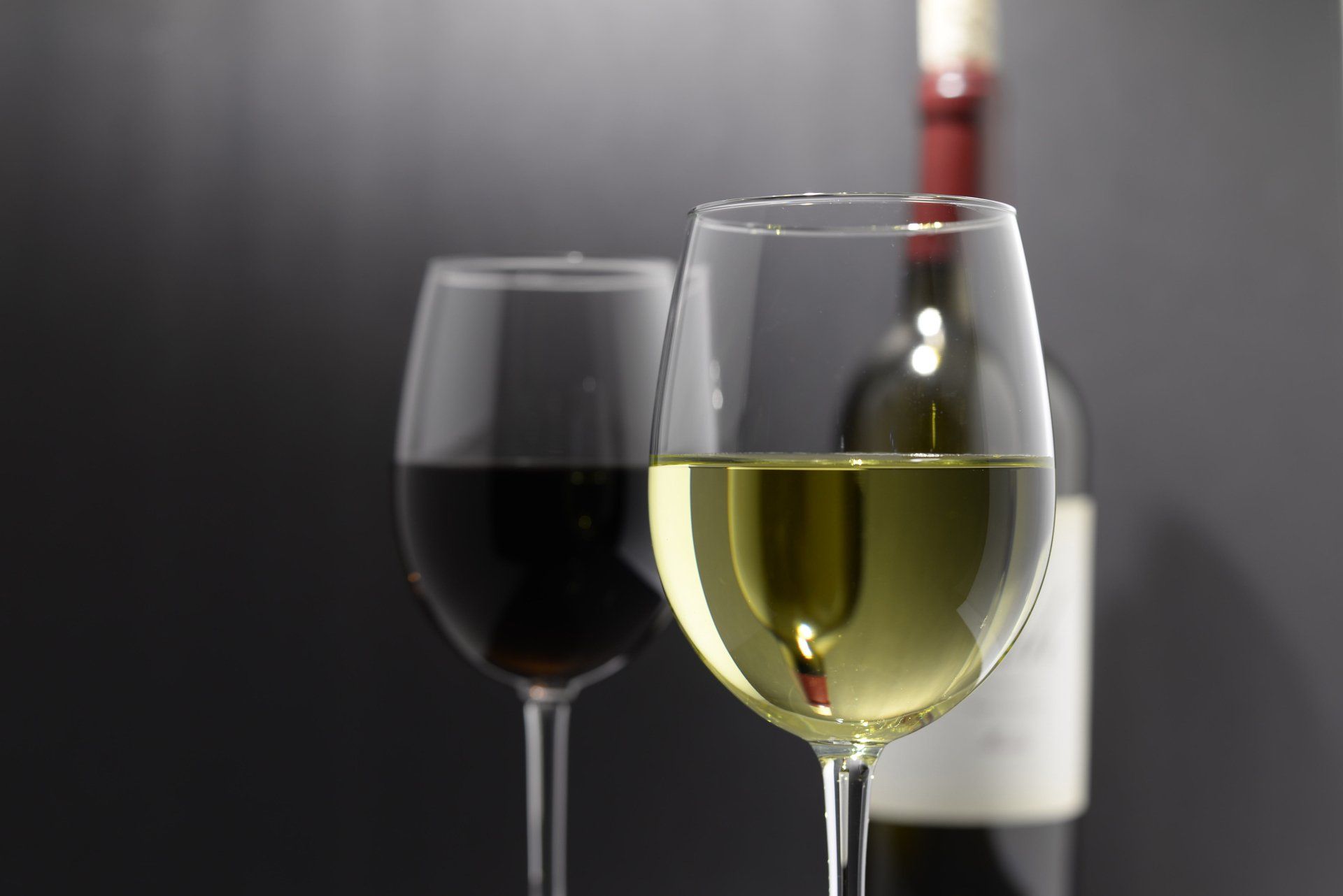 A bottle of wine is behind two glasses of wine