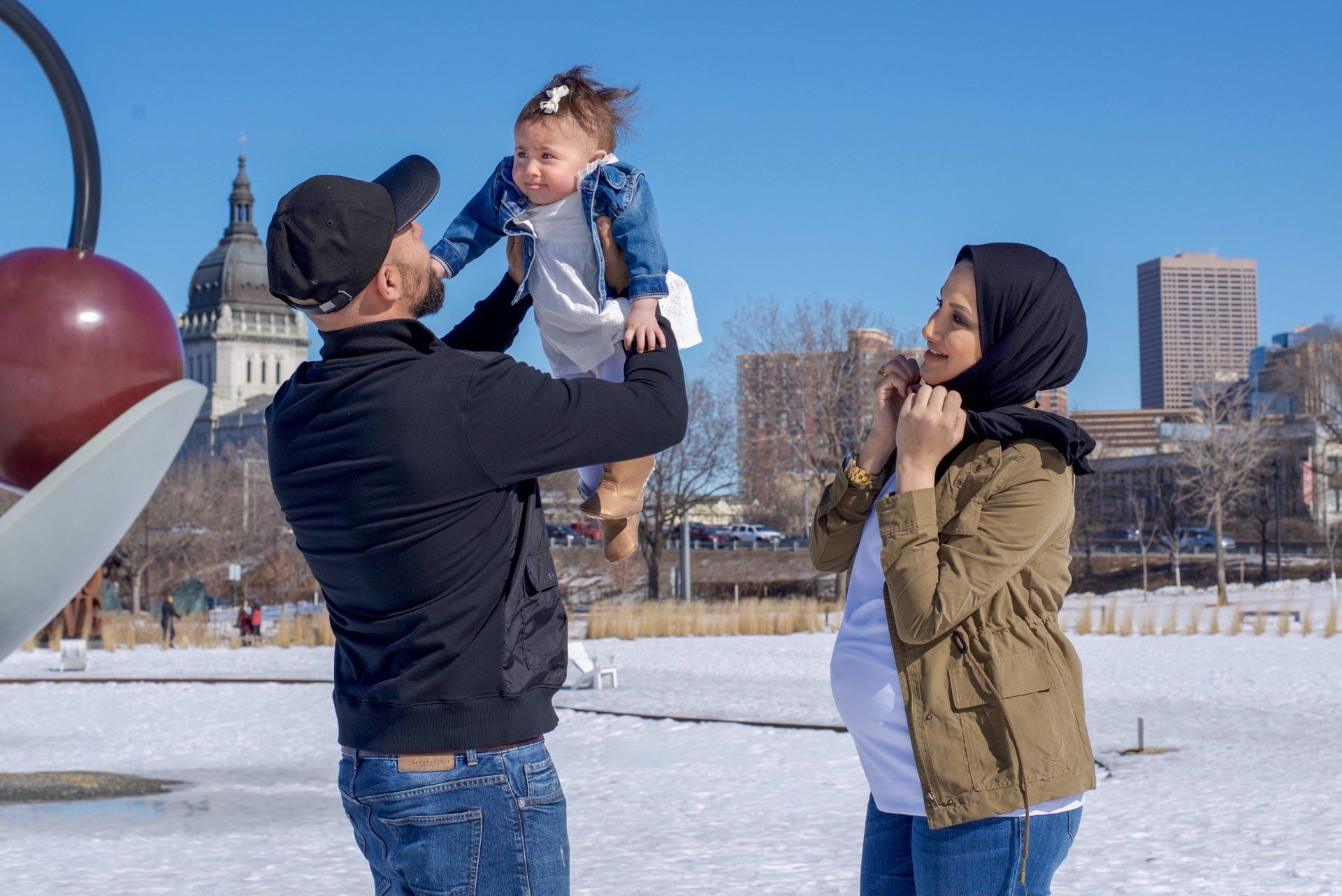 A man is holding a baby in the air while a woman looks on