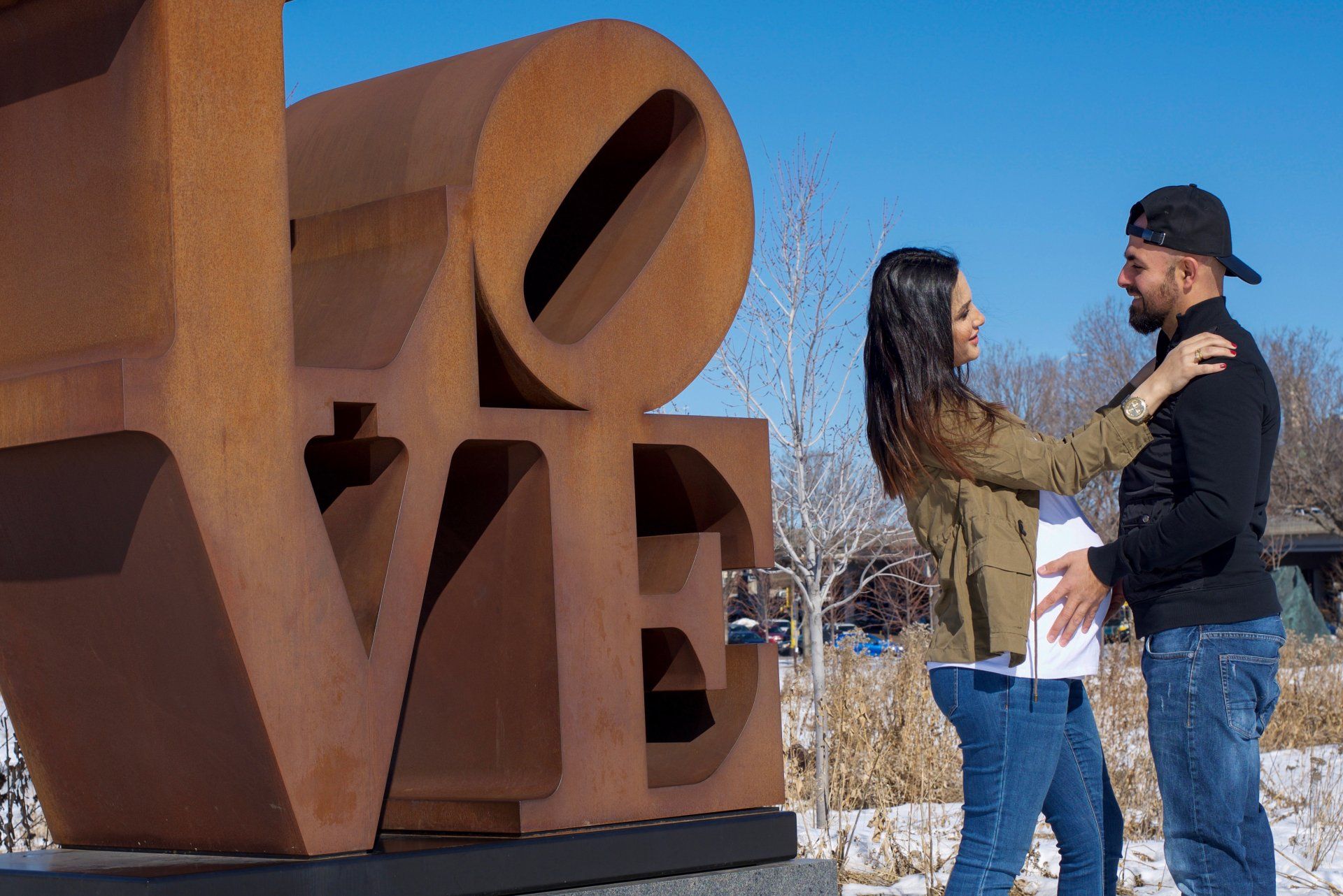 A man and woman are standing in front of a large love sculpture
